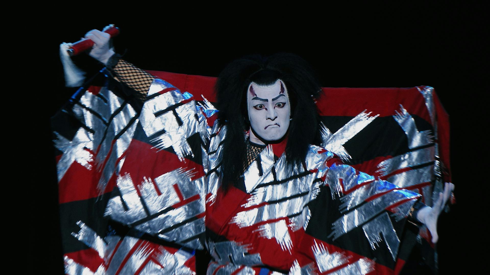 An actor does Kabuki in a white, black, and red robe.