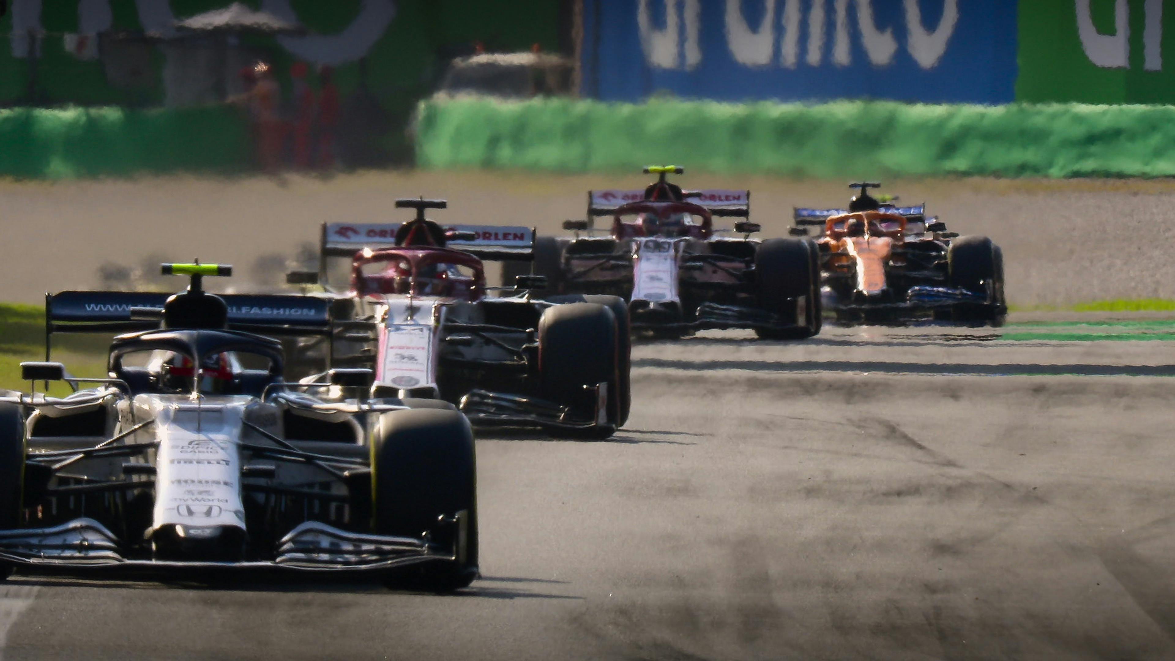 Some cars race down a grey pavement track. 