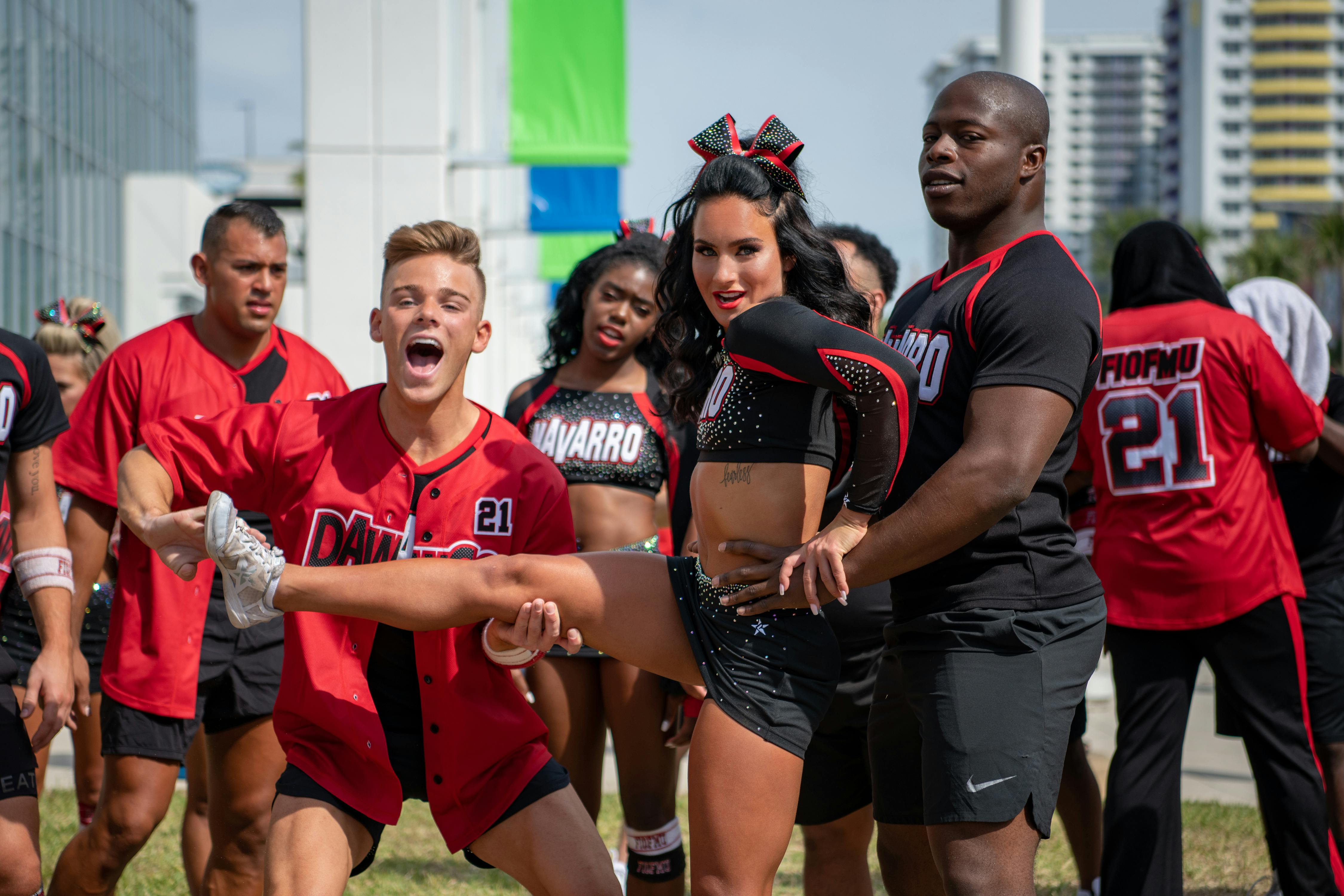 The Cheer cast prepare for a lift. They wear black and red uniforms.