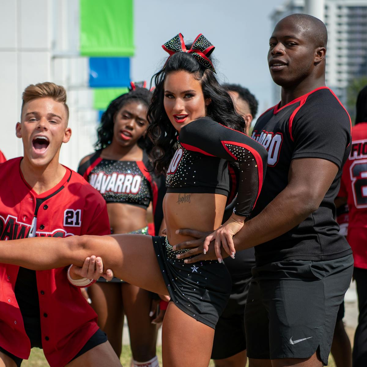 The Cheer cast prepare for a lift. They wear black and red uniforms.