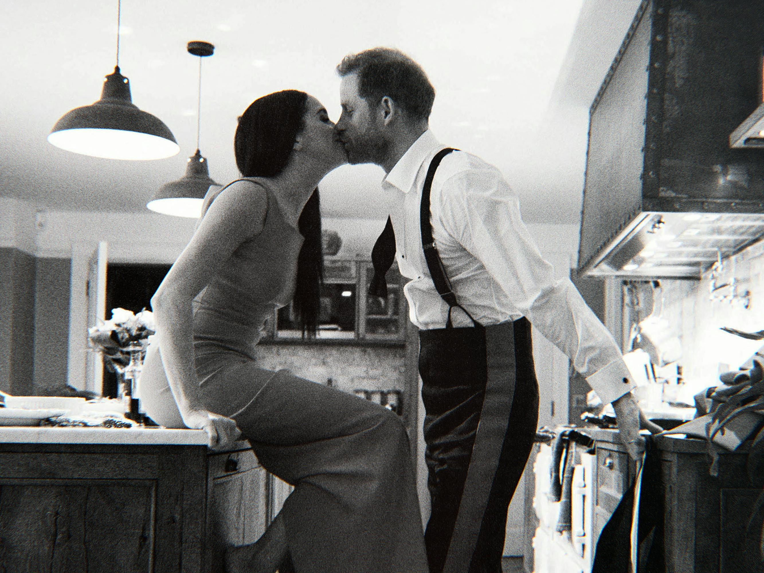 Meghan and Harry kiss in this black and white shot. Meghan sits on the counter and Harry wears suspenders.