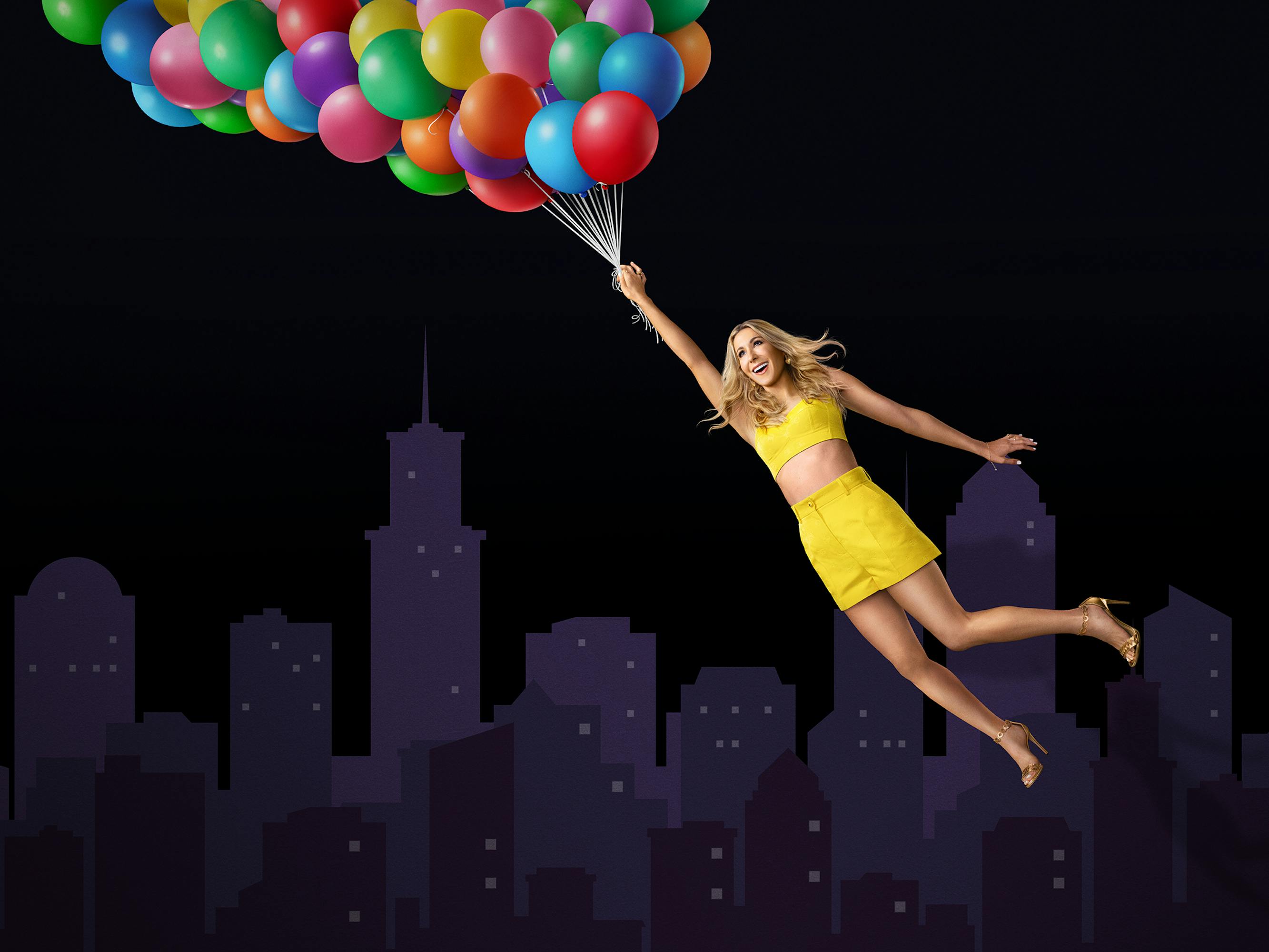 Nikki Glaser wears a yellow set and holds a bushel of balloons.
