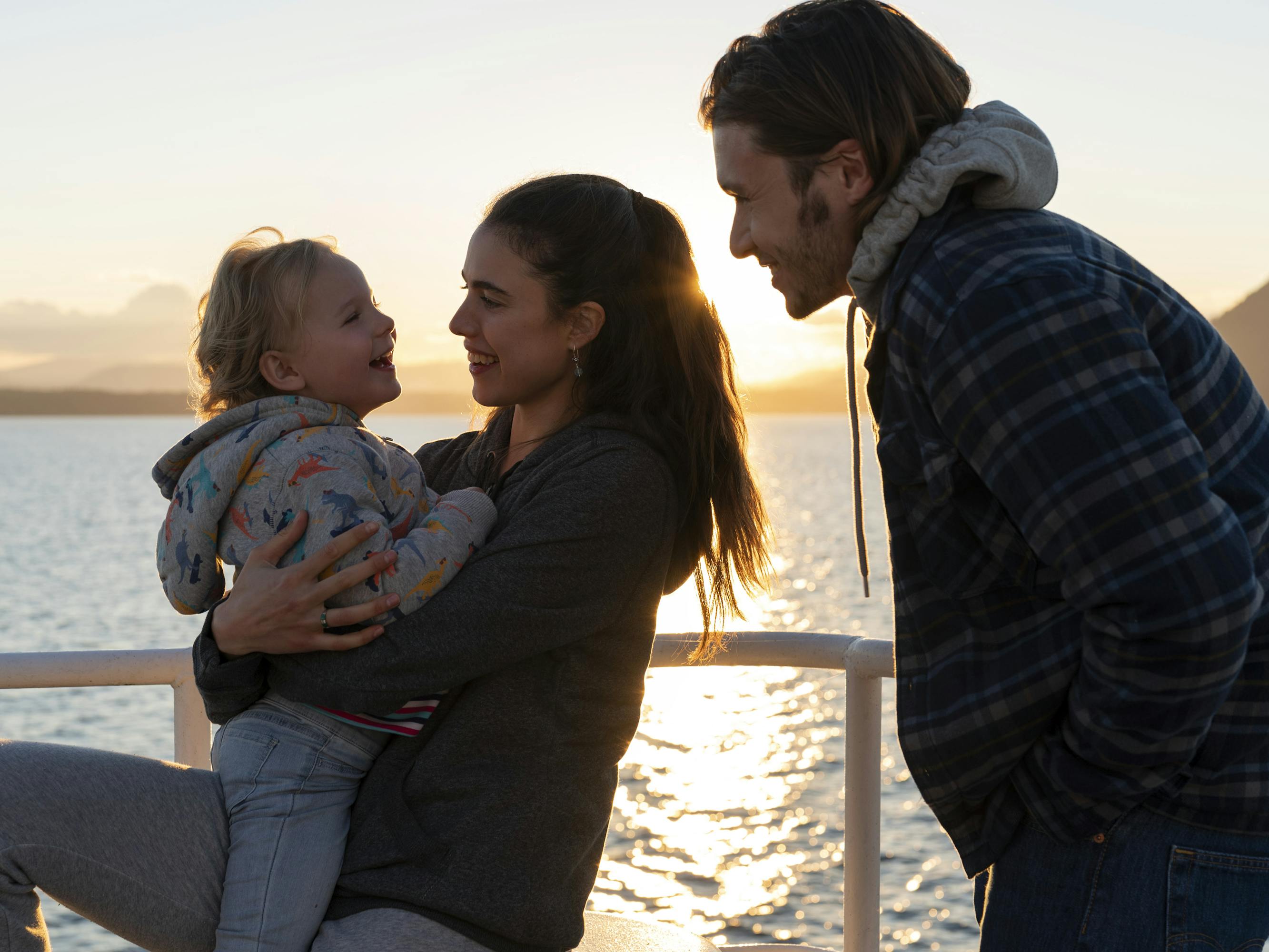 Maddy (Rylea Nevaeh Whittet), Alex Russell (Margaret Qualley), and Sean Boyd (Nick Robinson) stand on a boat against a setting sun.