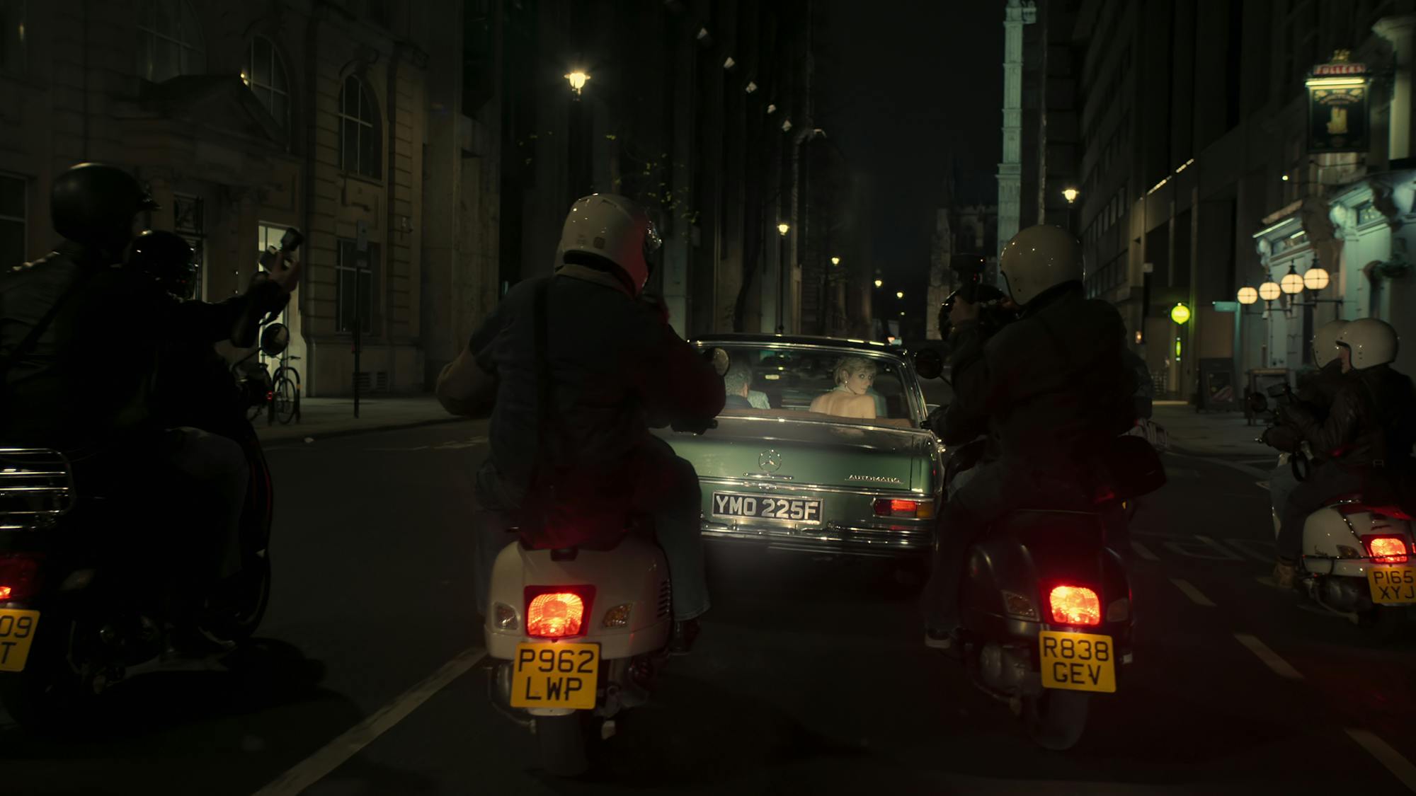 Princess Diana (Elizabeth Debicki) sits in a green car, getting followed by paparazzi on motorcycles.