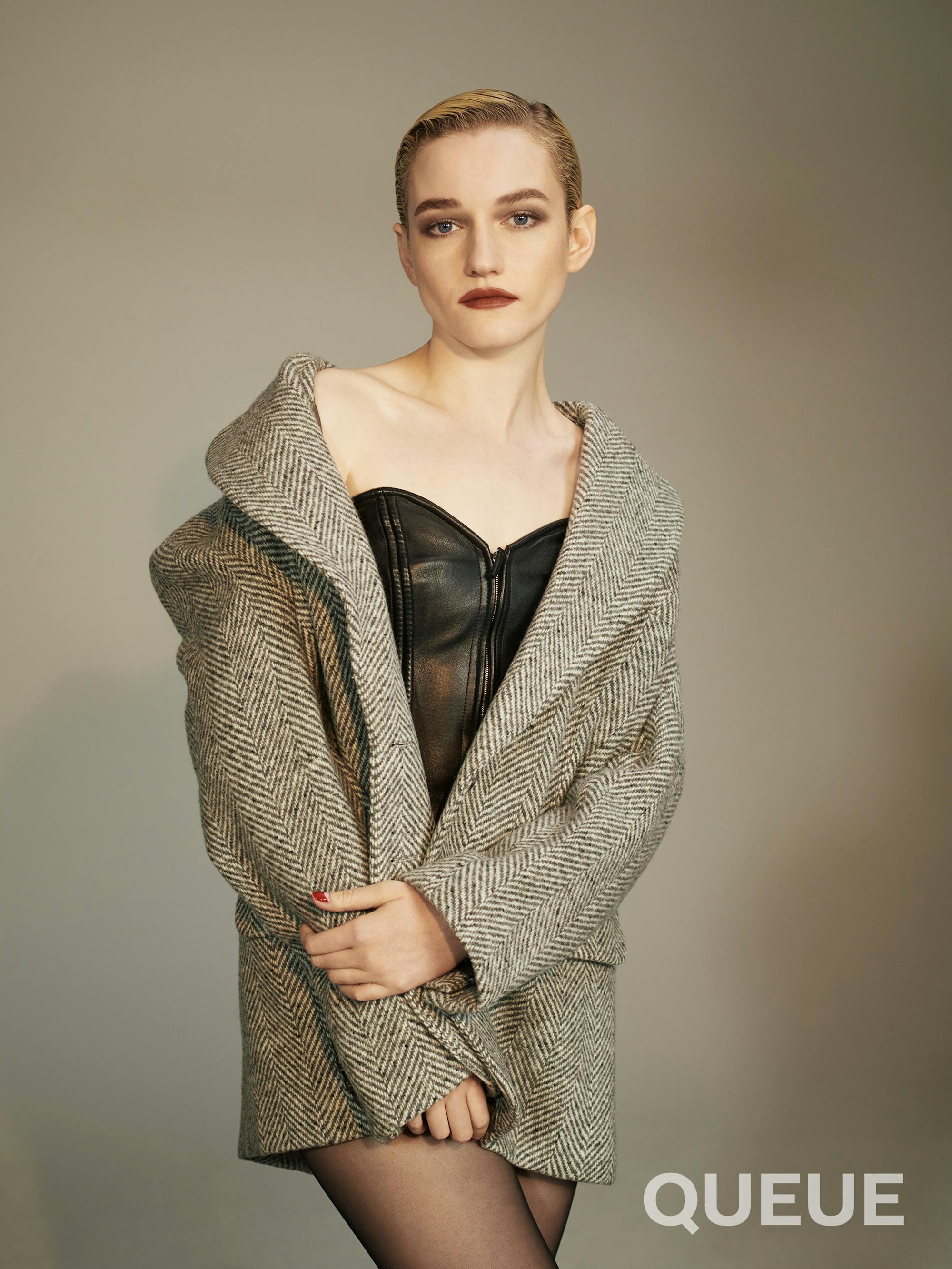 Julia Garner wears a black bustier and tweed jacket and tights.