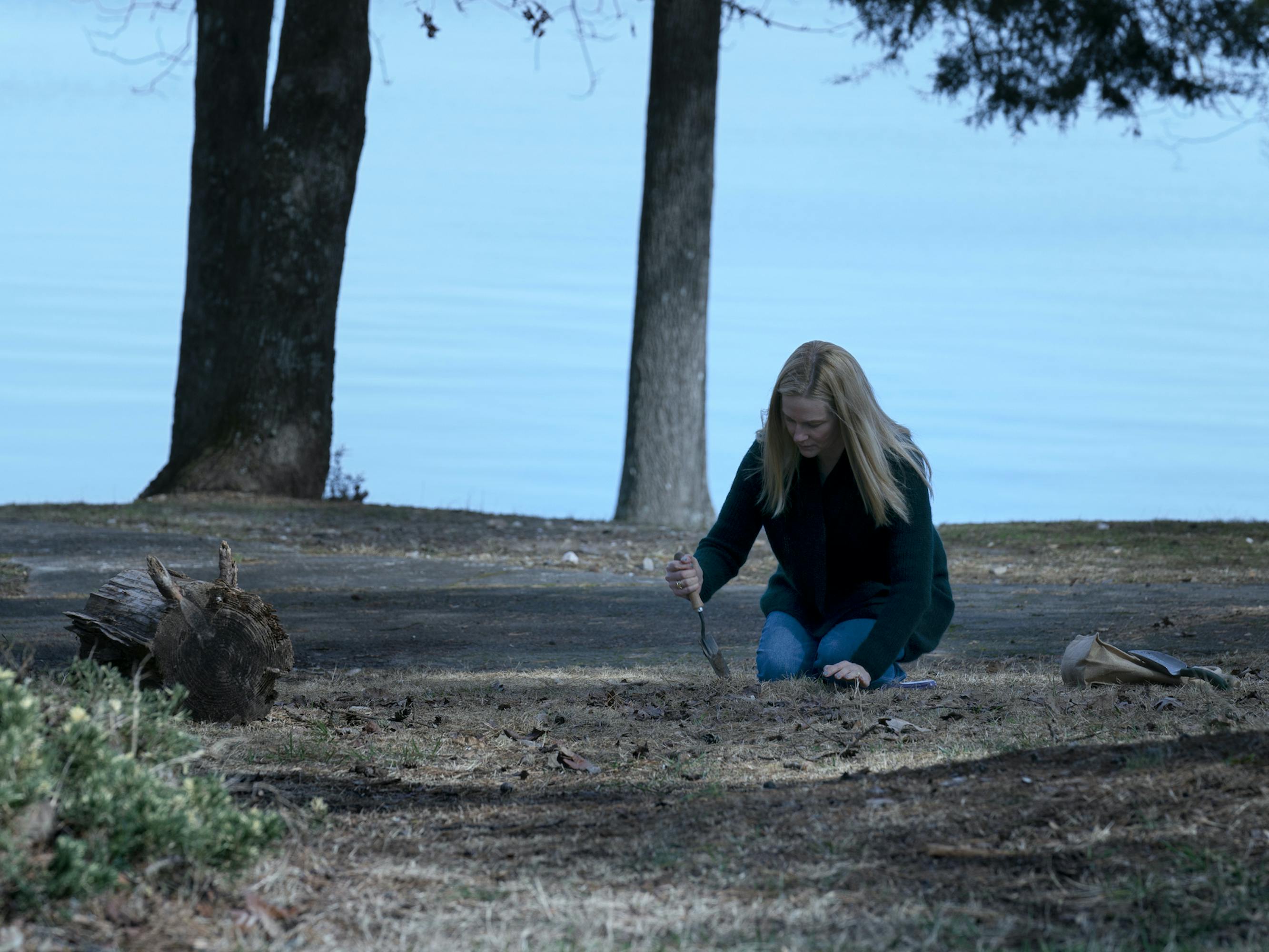 Wendy Byrde (Laura Linney) crouches in the dirt beside the water. What is she digging up, or else, burying?