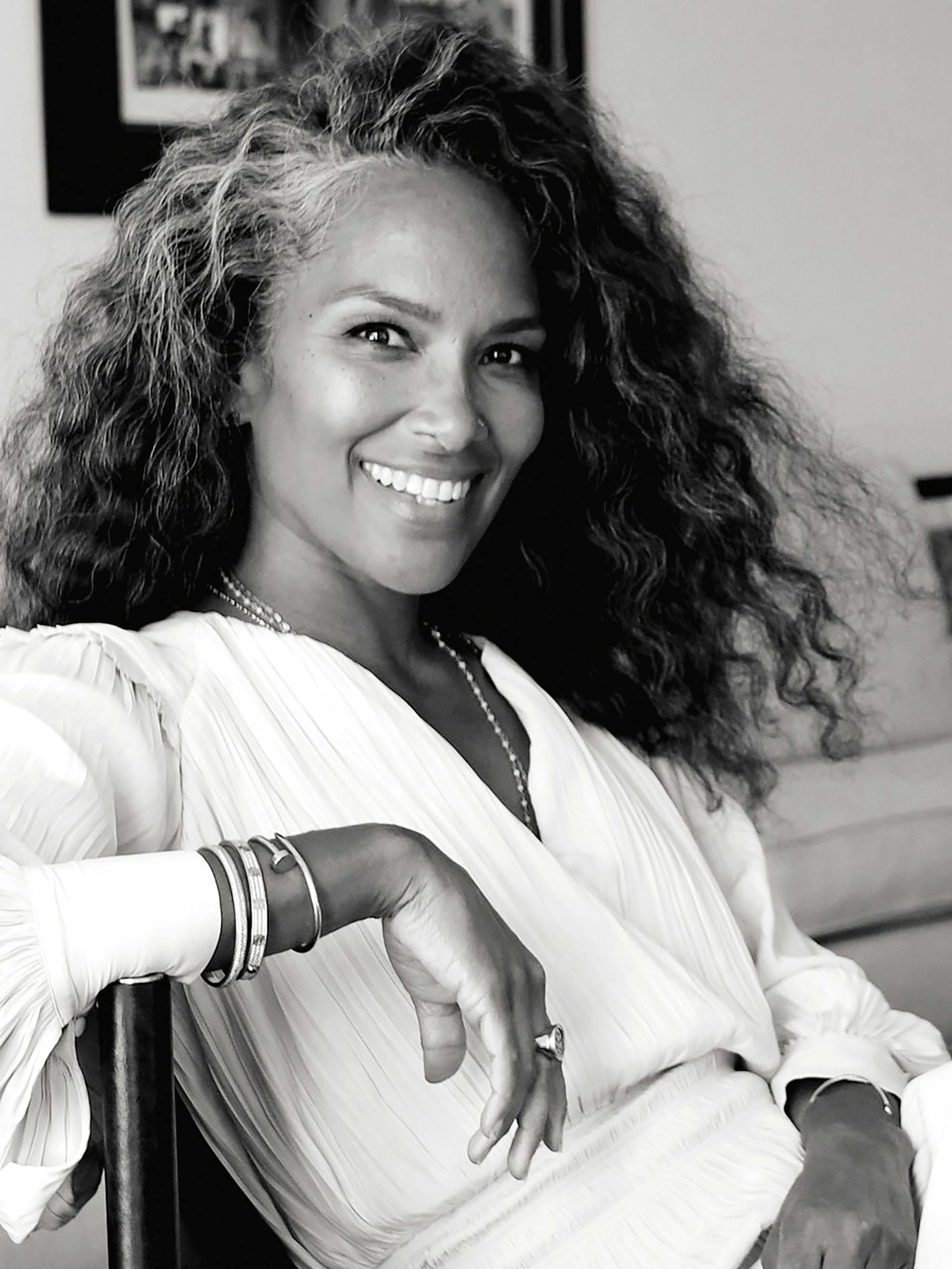 Mara Brock Akil wears a white shirt and necklace and smiles widely.