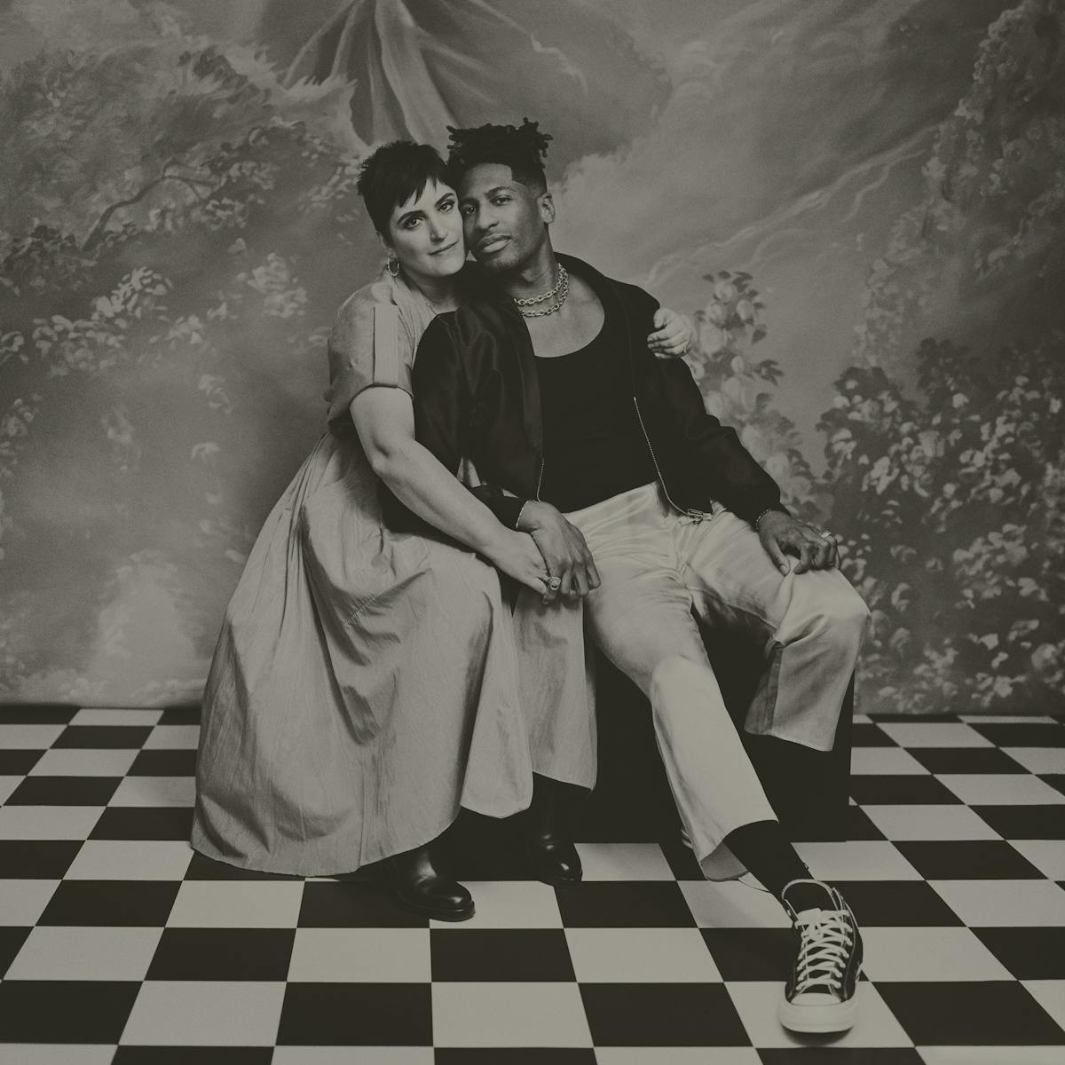 Suleika Jaouad and Jon Batiste smile in a black-and-white picture sitting on a black-and-white checkered floor.