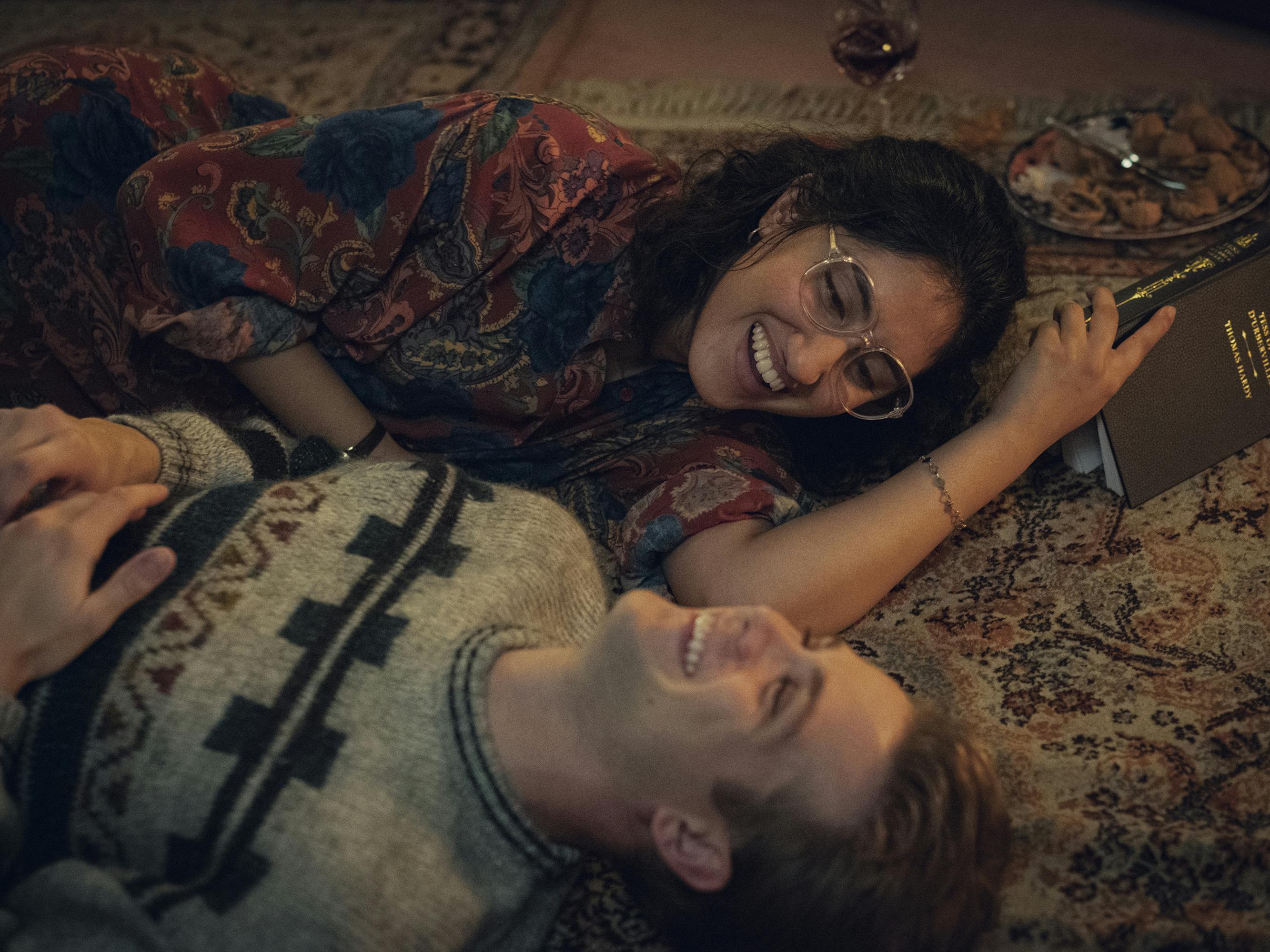Dexter Mayhew (Leo Woodall) and Emma Morley (Ambika Mod) lie on a rug laughing. 