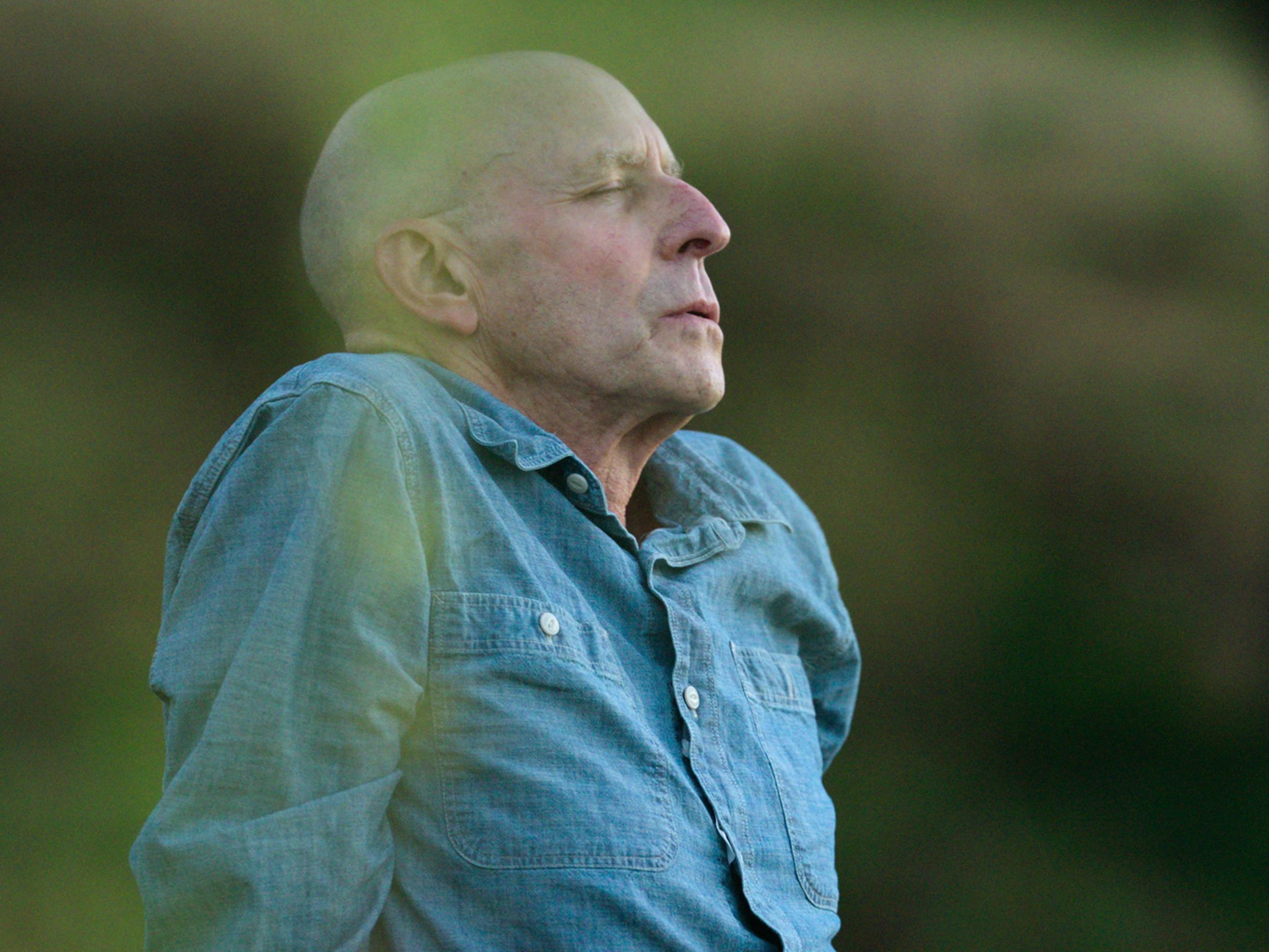 Michael Pollan wears a denim shirt and sits in a grassy field.