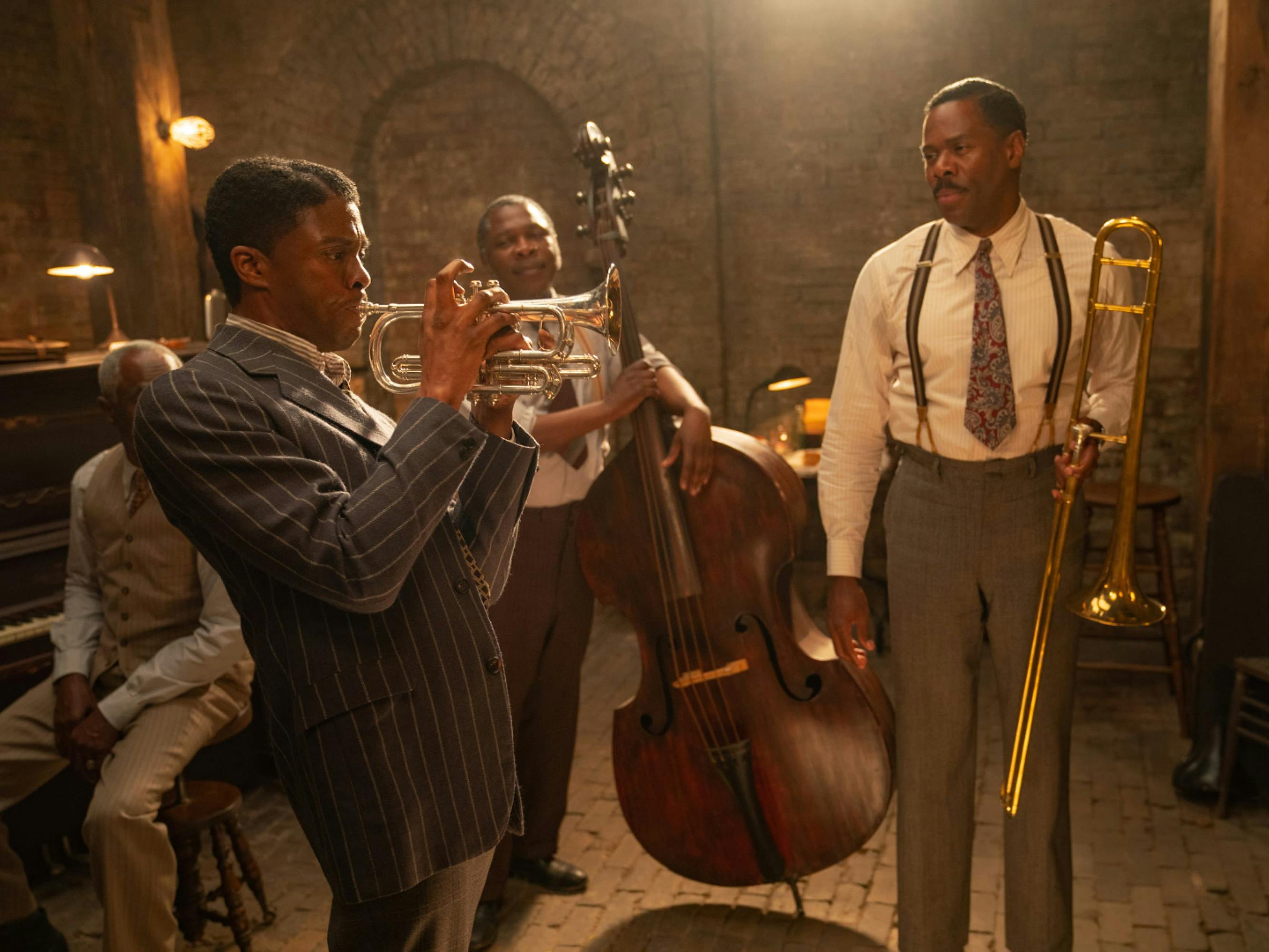 Boseman as Levee. He wears a striped suit and plays the trumpet as the rest of the band looks on. 