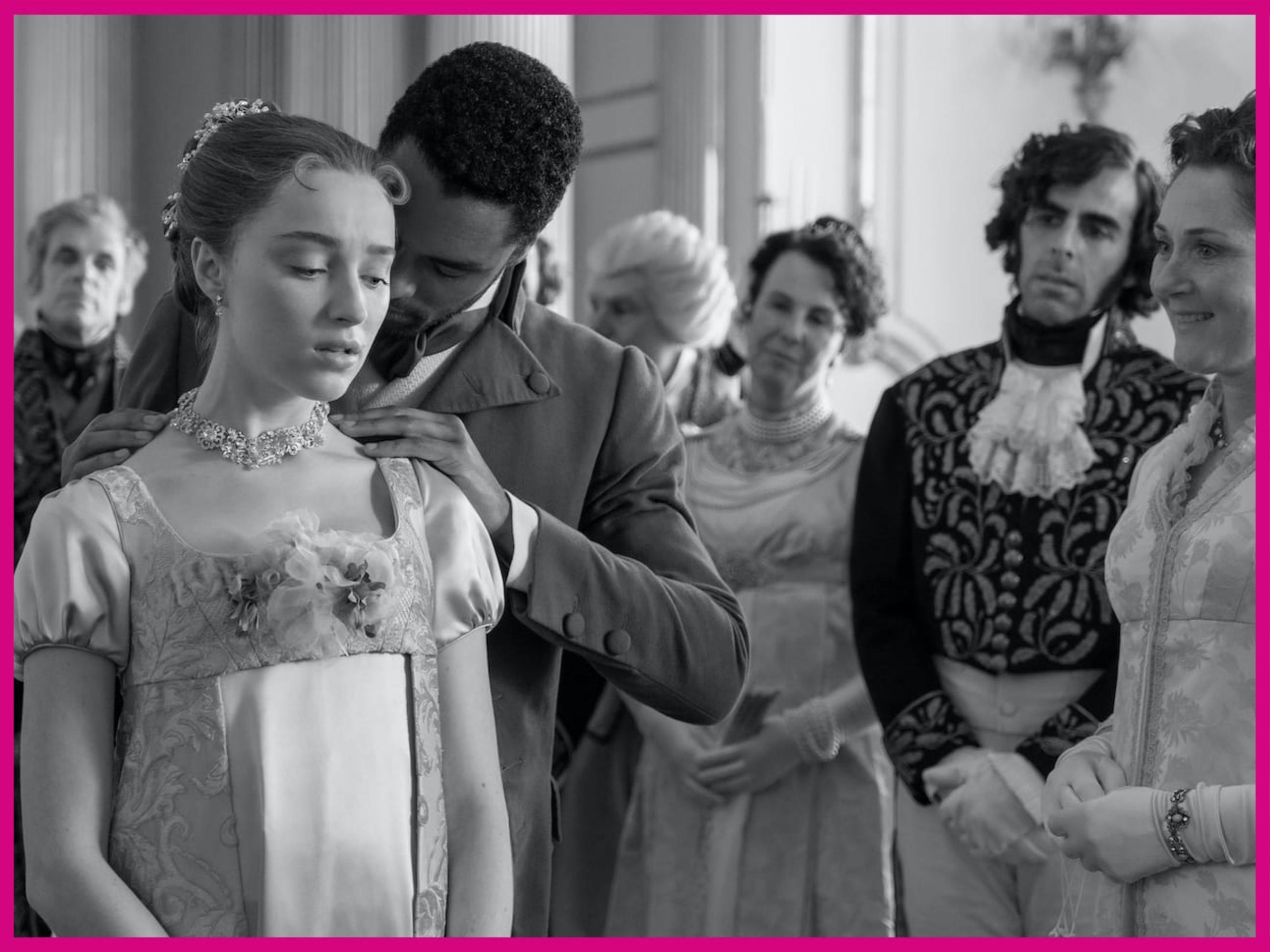 Daphne Bridgerton (Phoebe Dynevor) and Simon Basset (Regé-Jean Page) stand together as Basset clips a necklace around Daphne’s neck. Daphne wears a light blue dress, and Basset wears a brown coat. They are surrounded by family who look on eagerly.