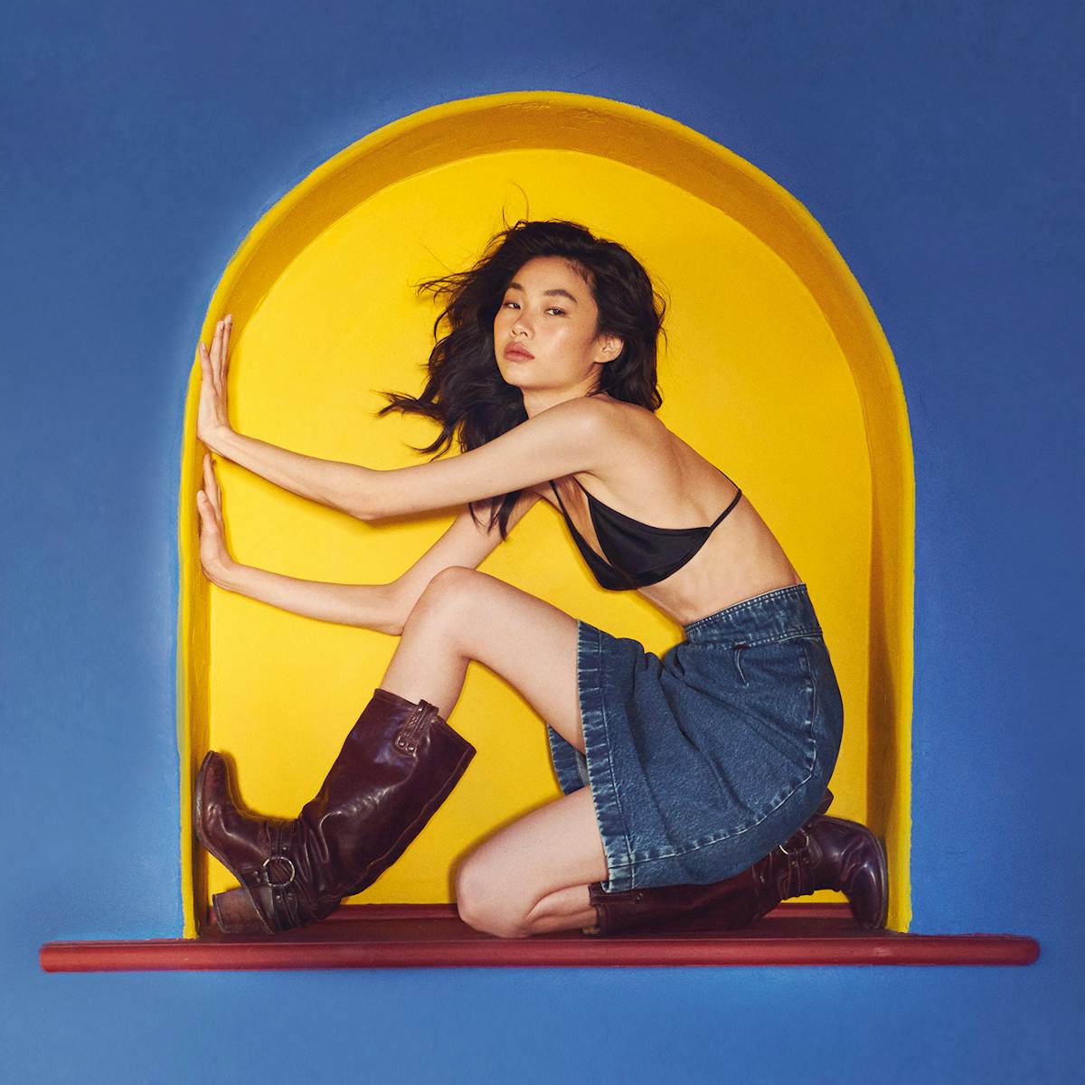 Jung Ho-yeon sits in a yellow nook on a blue wall. 