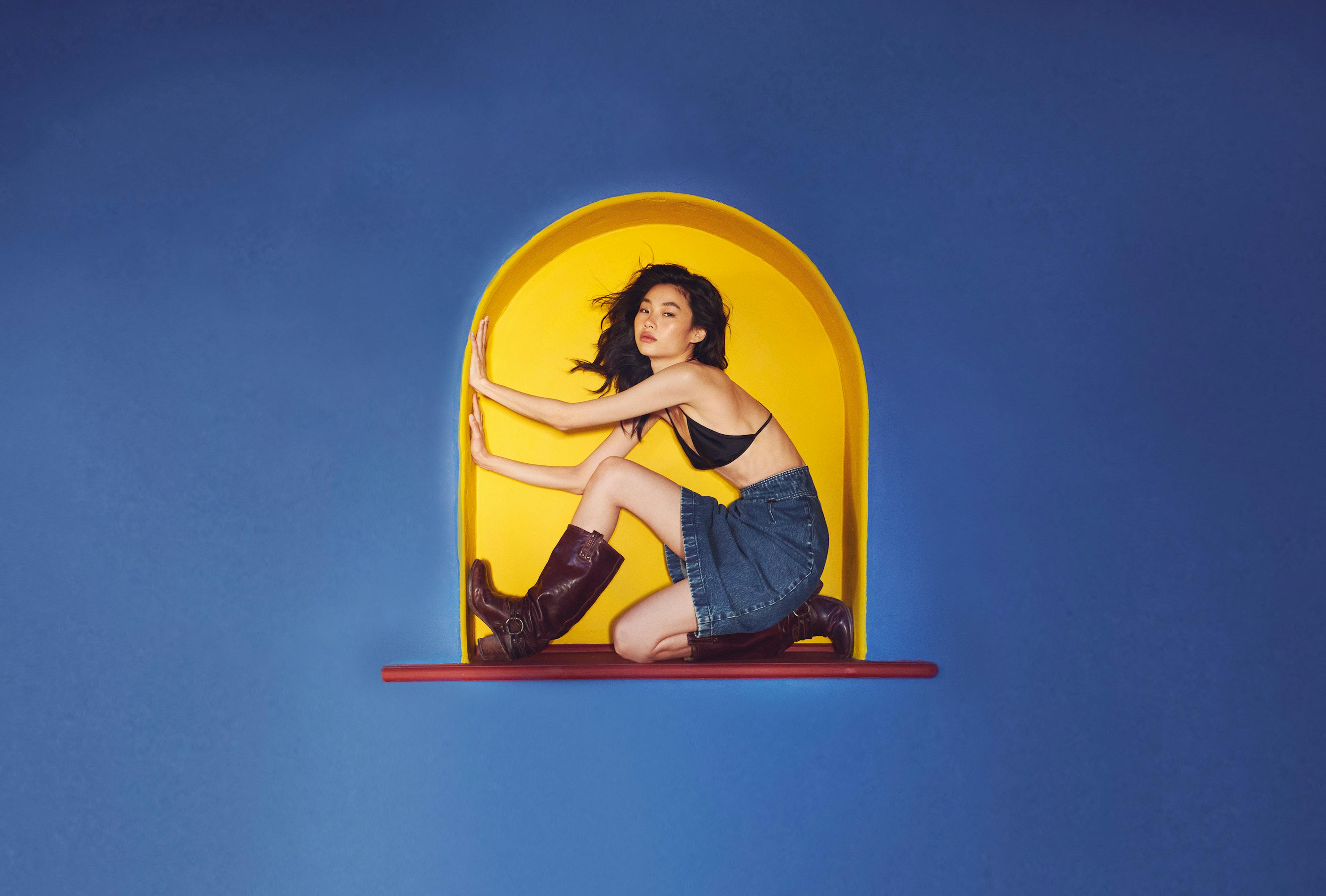 Jung Ho-yeon sits in a yellow nook on a blue wall. 