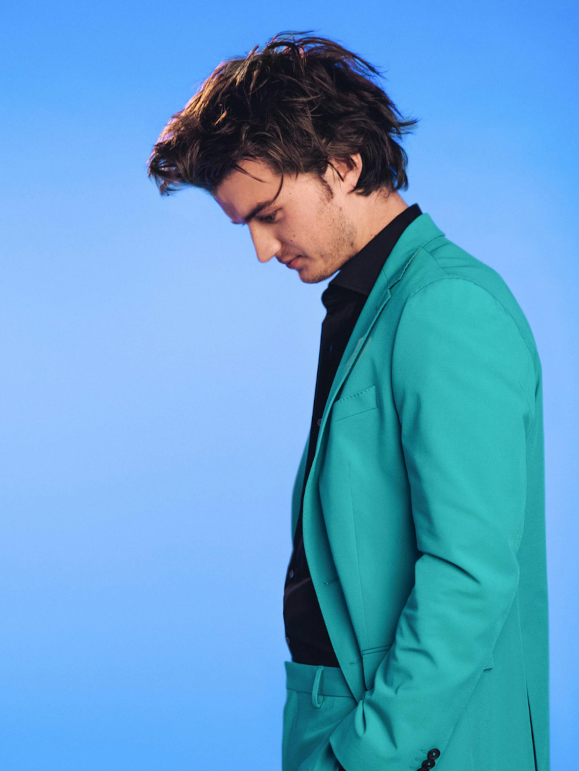 Joe Keery of Stranger Things poses in front of a sky blue background.