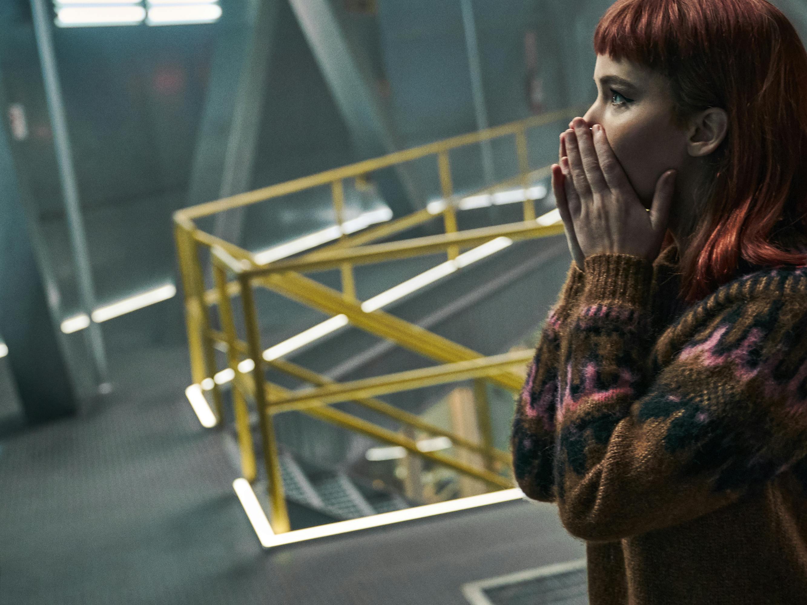 Jennifer Lawrence wears a patterned sweater and red wig, covering his mouth with her hands in shock.