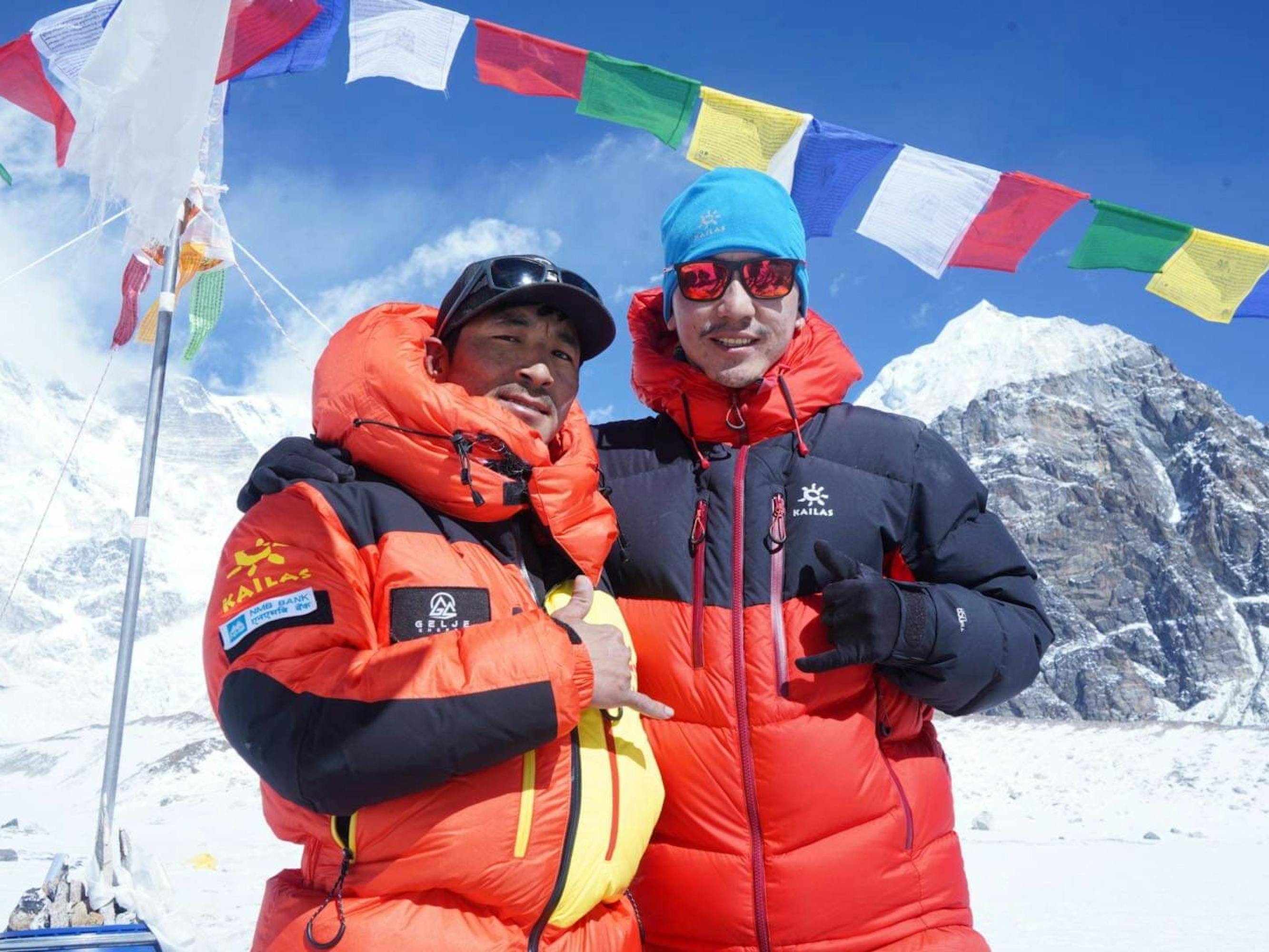 Geljen Sherpa wears orange and stands against a blue sky dotted with flags. 