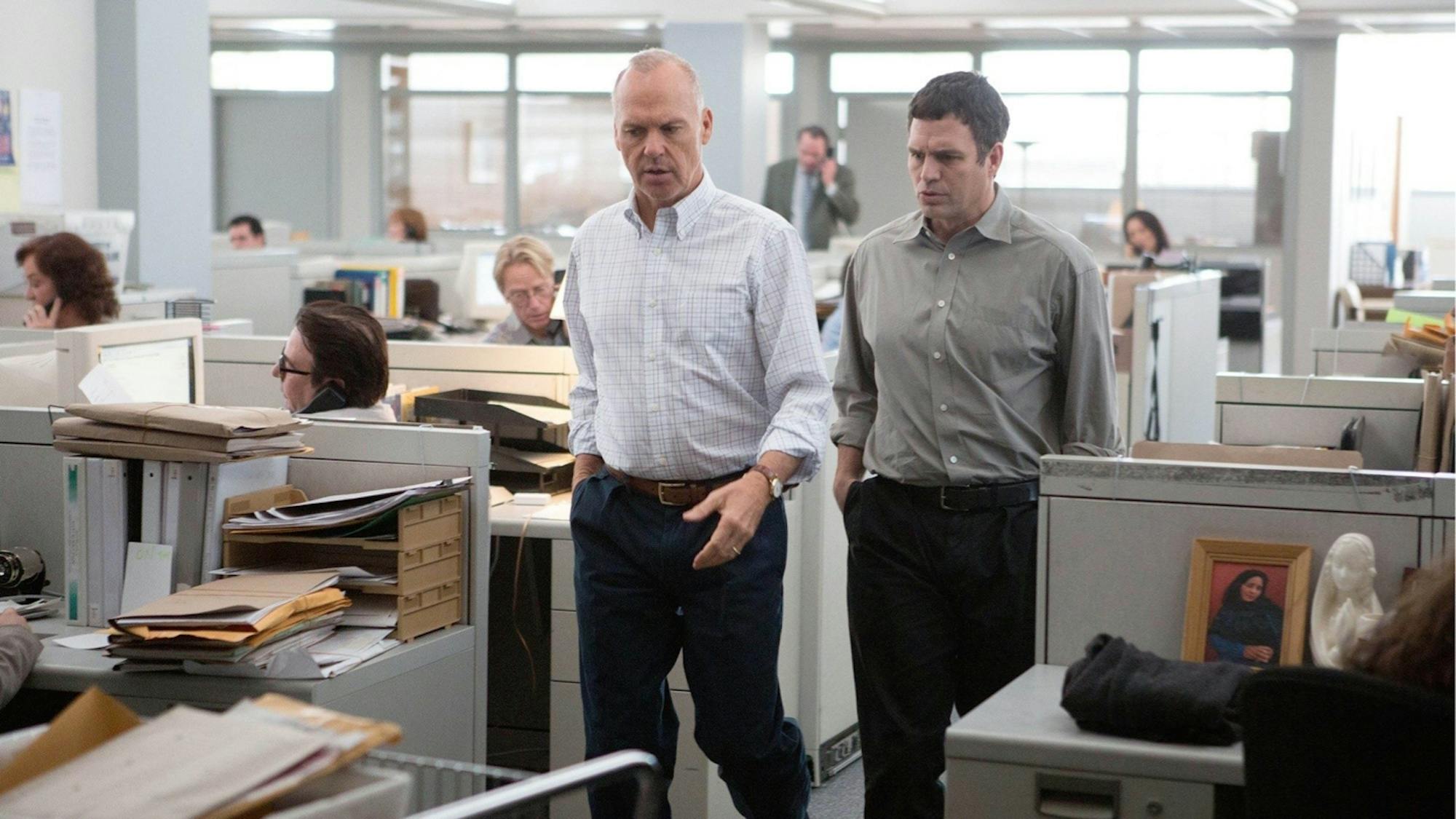 Walter Robinson (Michael Keaton) and Mike Rezendes (Mark Ruffalo) in Spotlight stand in an office space walking between cubicles.
