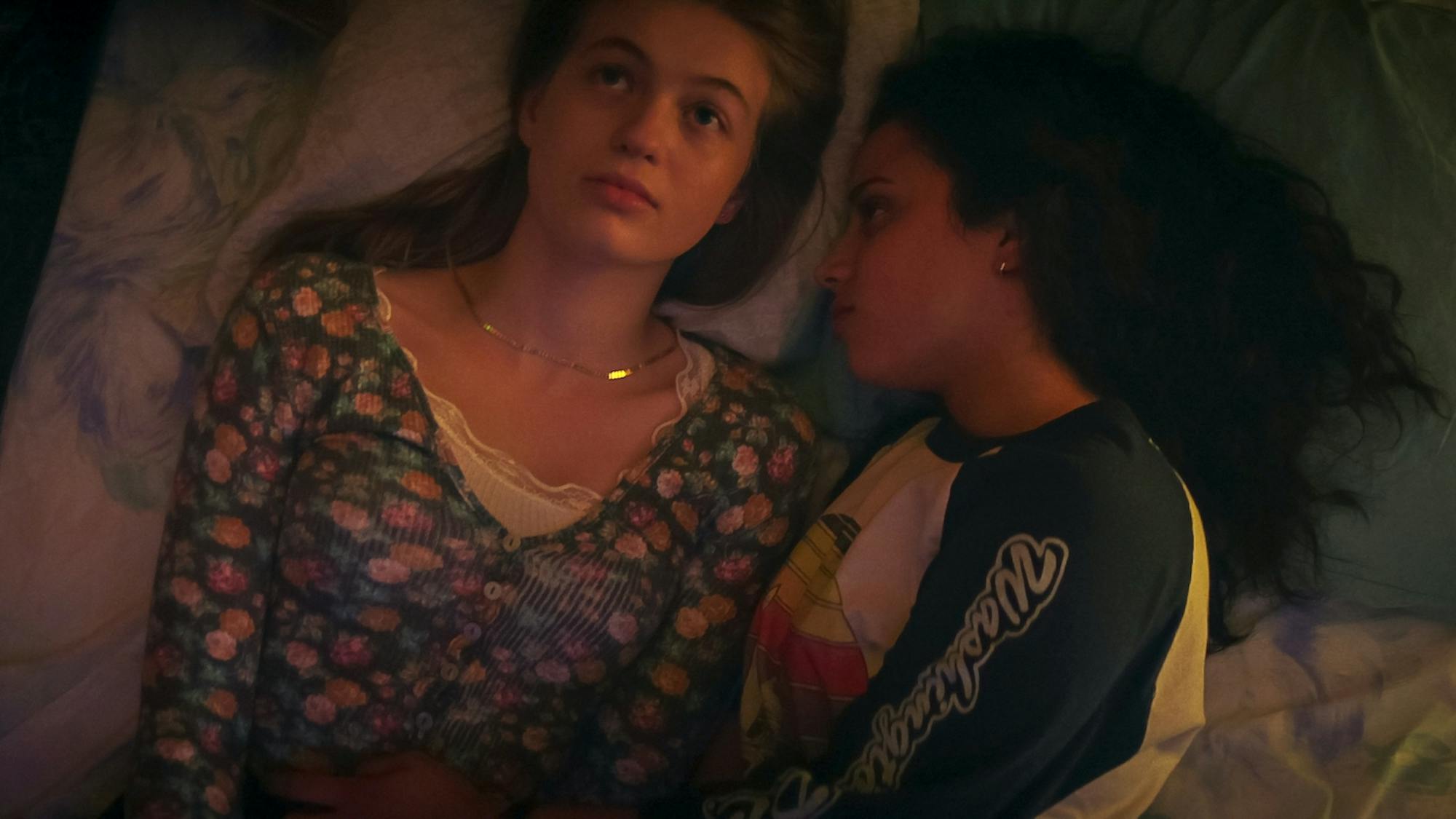 Sam (Olivia Scott Welch) and Deena (Kiana Madeira) lie in bed, lit by warm light.