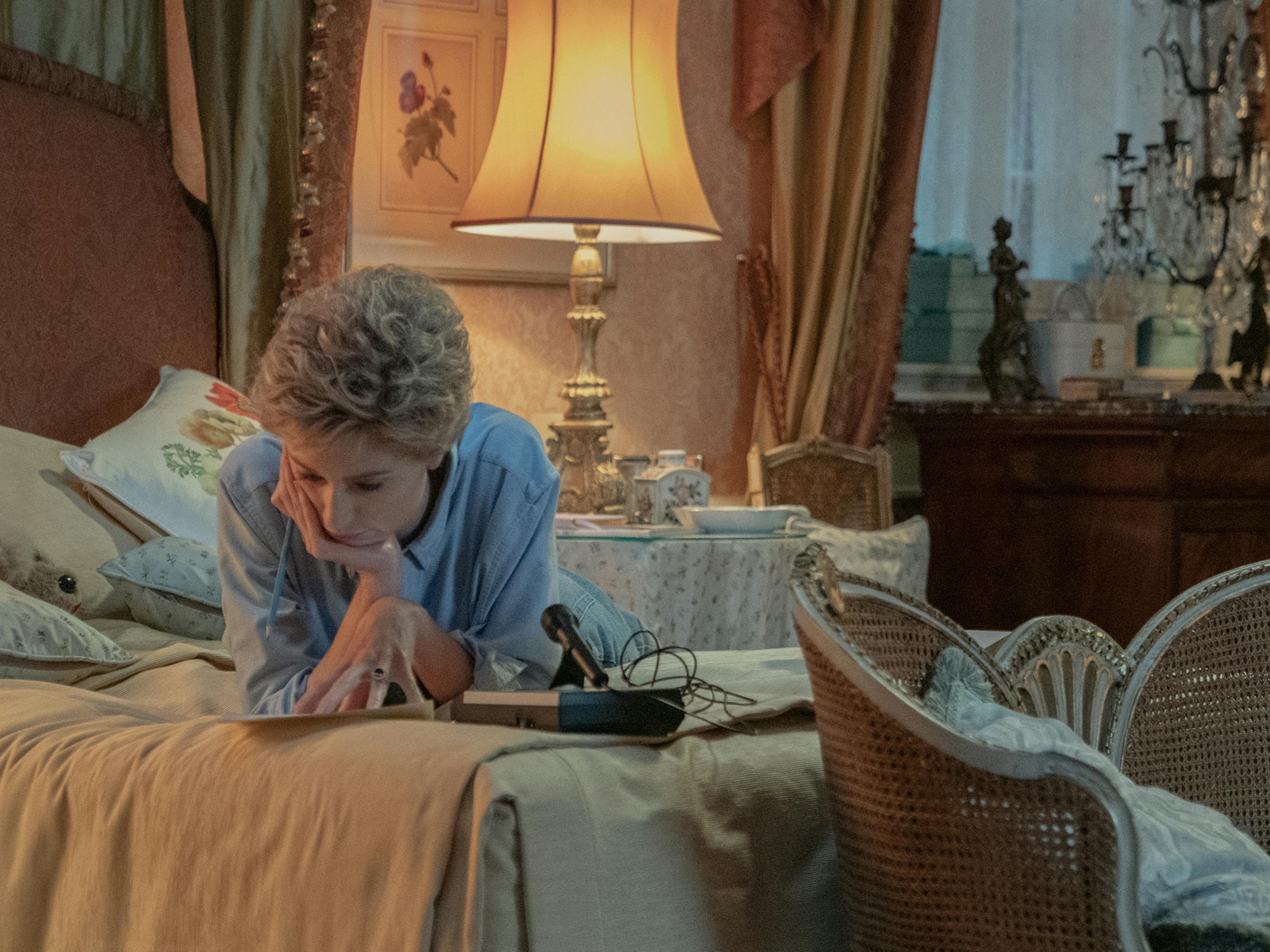 Princess Diana (Elizabeth Debicki) reads the newspaper while lying on her bed.