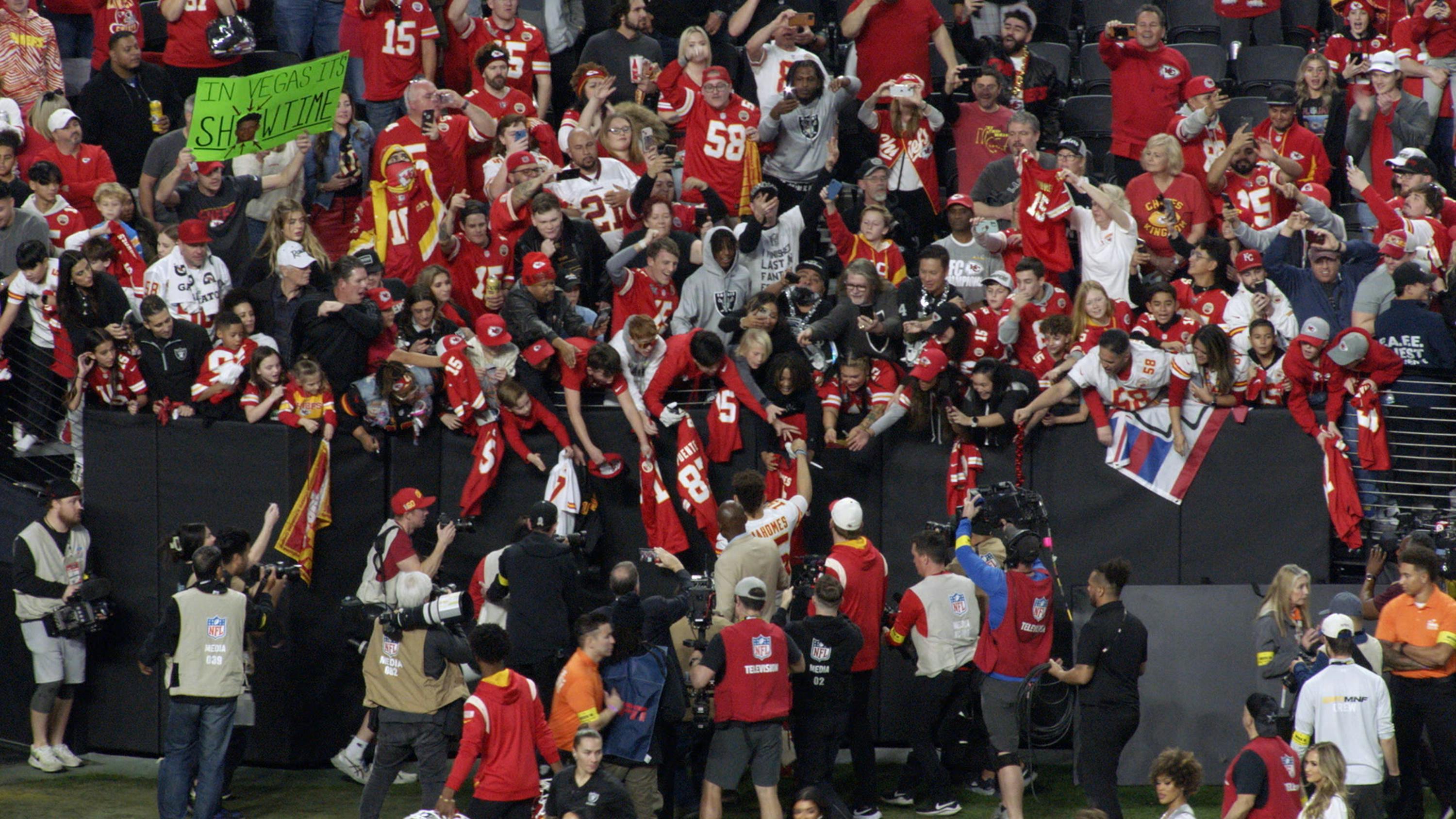 A crowd of fans wearing red jerseys greet a player as he walks off the field