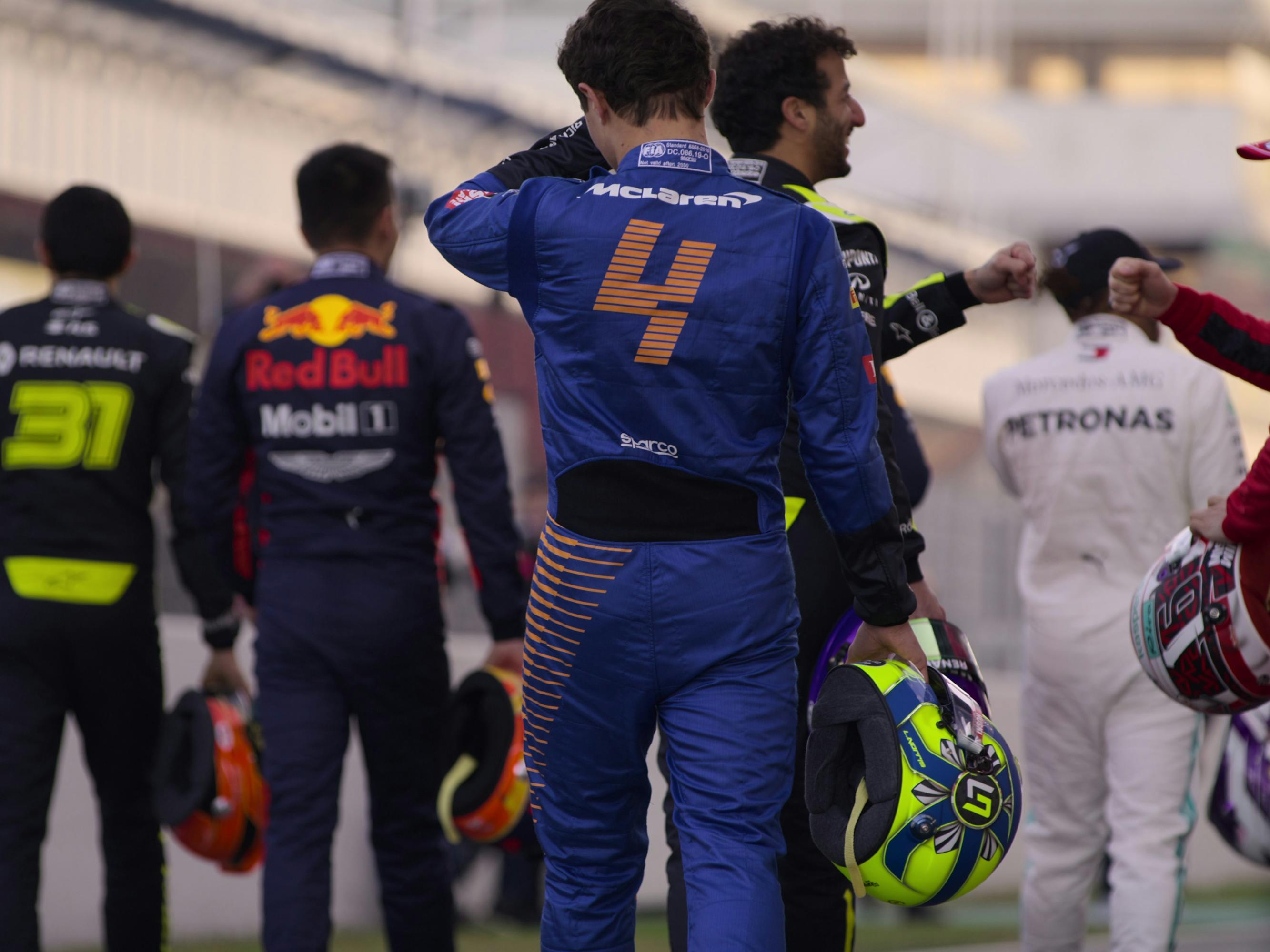 Formula 1 drivers stand with their backs to the camera.