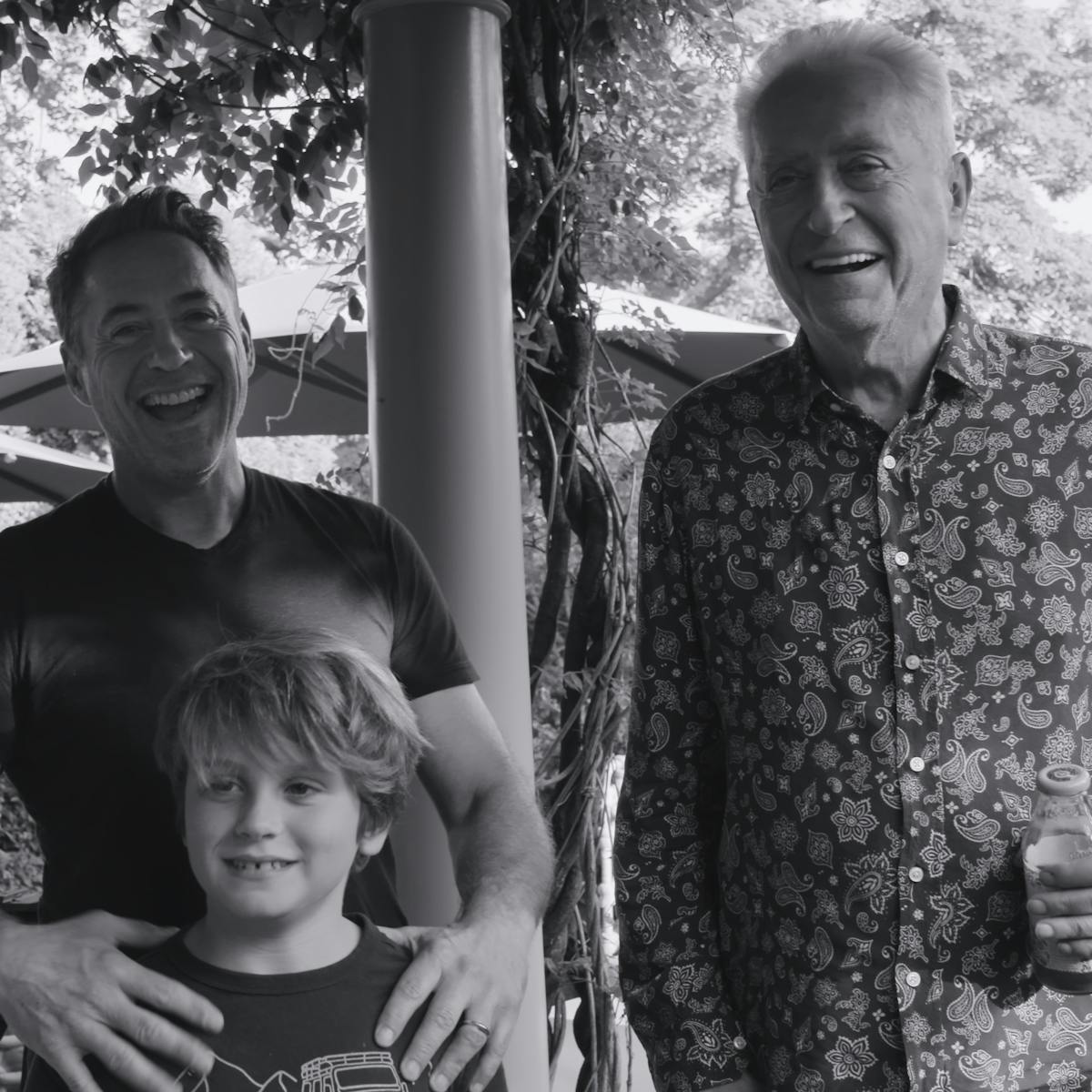 Robert Downey Jr., Exton, and Robert Downey Sr. stand together smiling in this black-and-white photo.