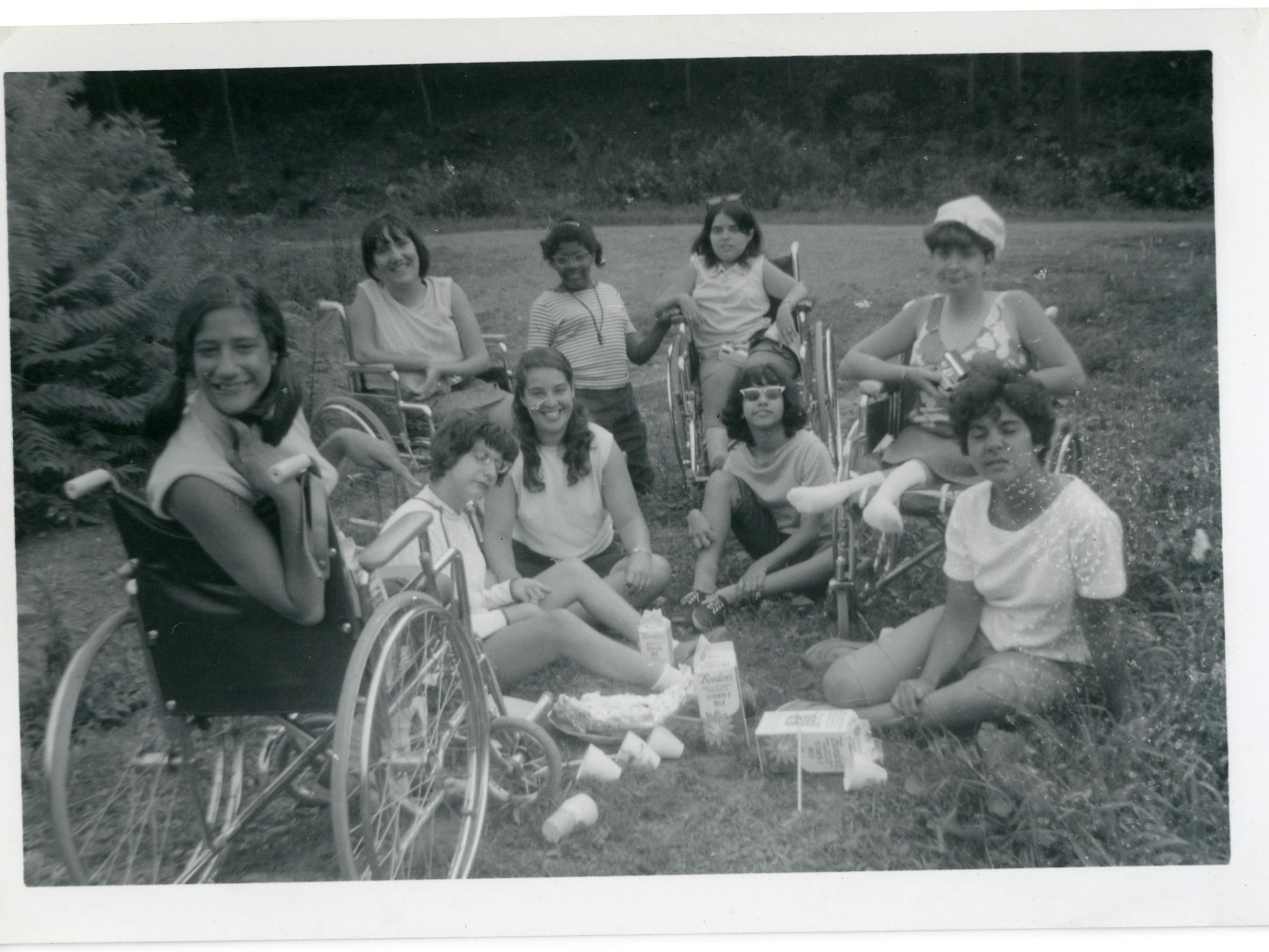 In an old photograph, teens sit in a circle on the grass, enjoying a summer day.