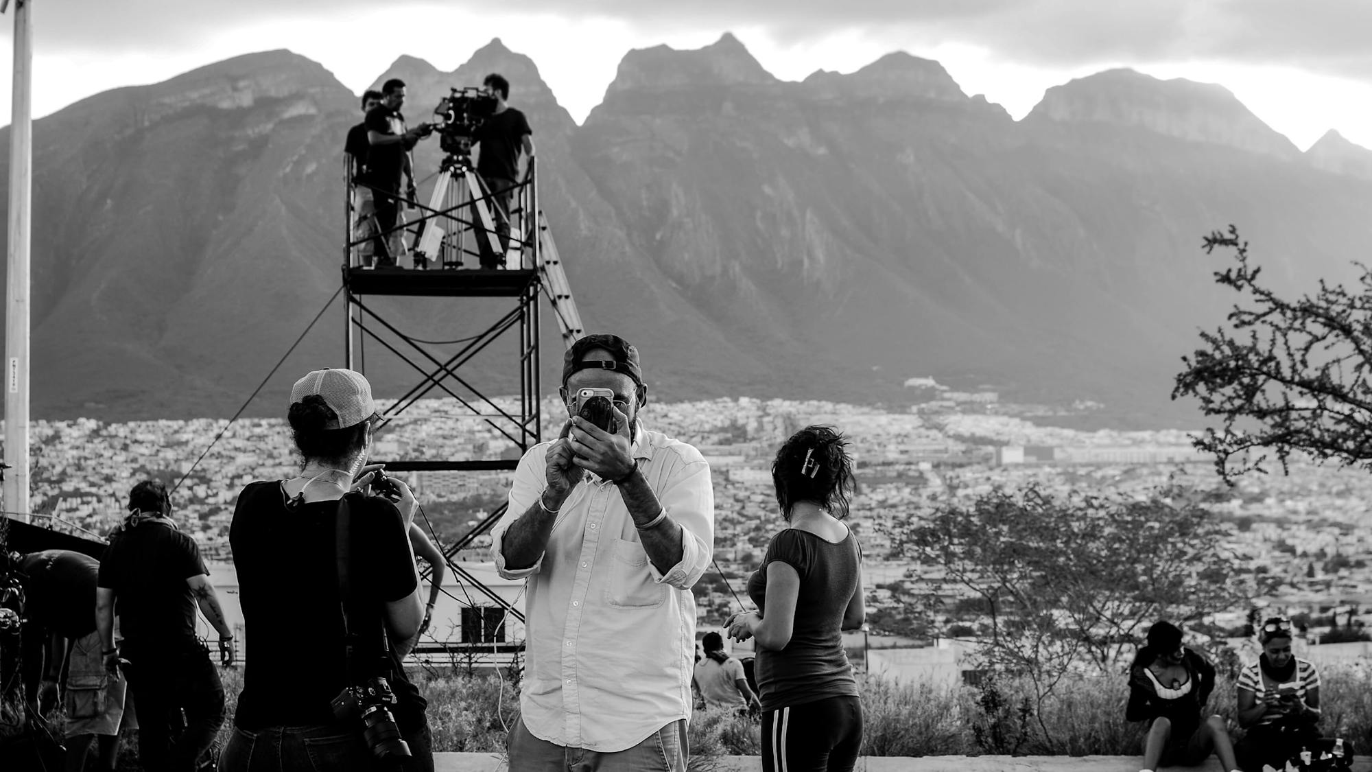 Frías de la Parra holds his camera up to his eye. Behind him, his crew prepares for a scene set against the striking mountains of Monterrey.