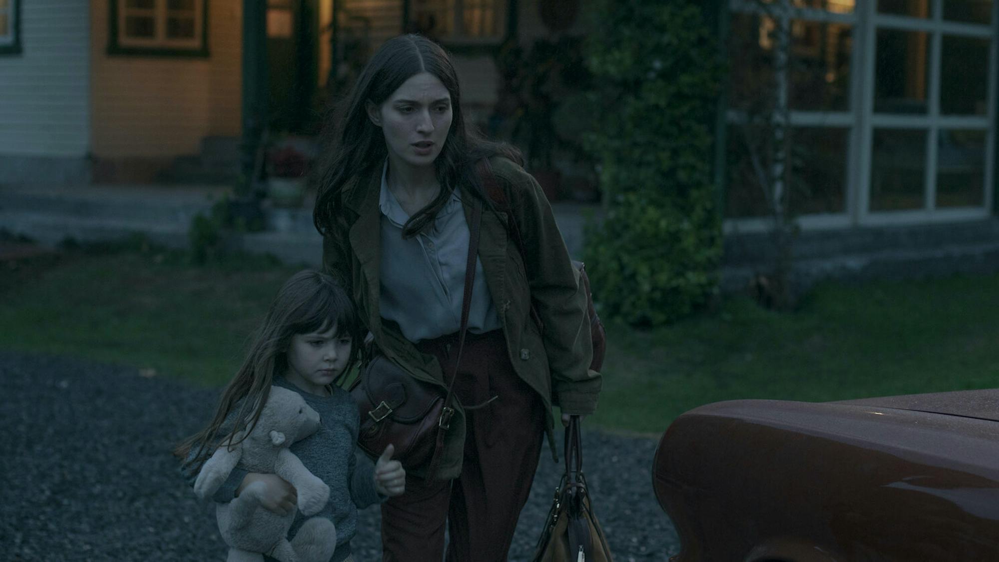 Nina (Guillermina Sorribes Liotta) and Amanda (María Valverde) rush to a red car at dusk. Nina clutches a bear while her mom carries two brown leather bags.
