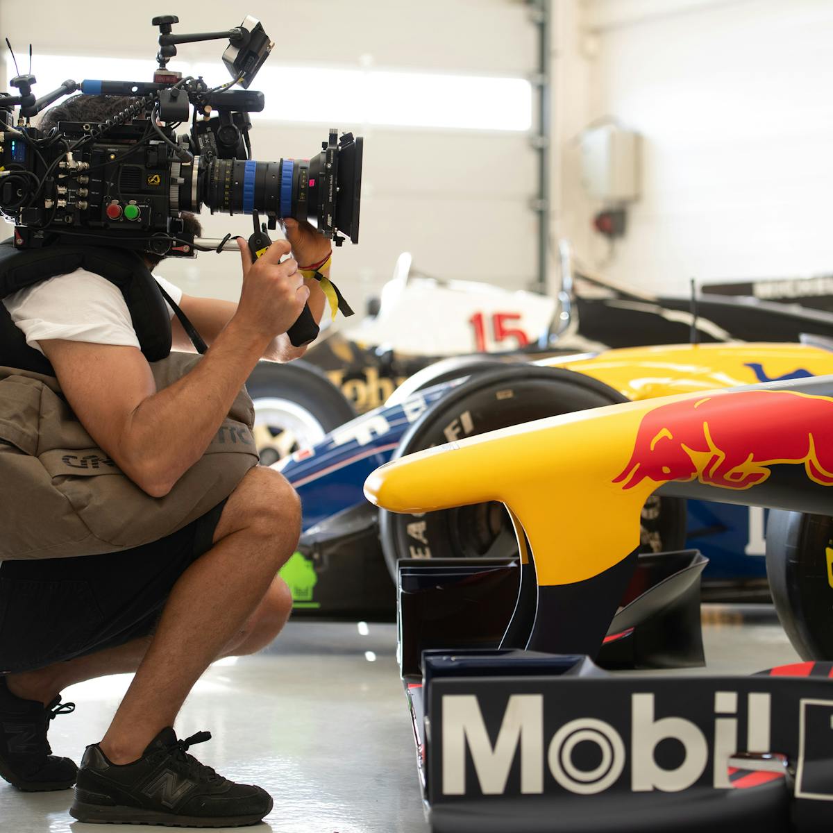 Behind the scenes of Formula 1: Drive to Survive. A person holding a camera crouches next to a yellow, red, and black car with Mobil 1 on its side.