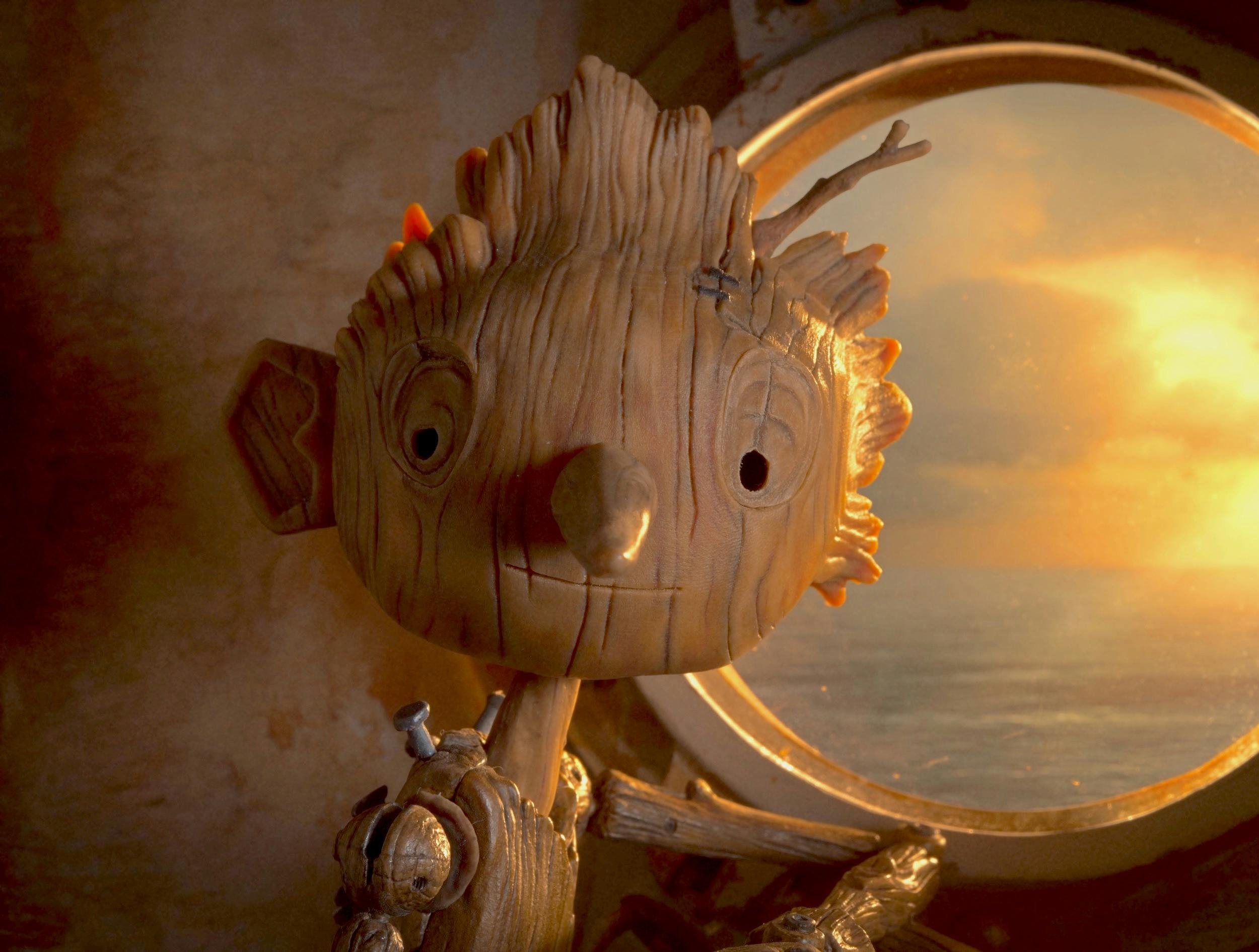 Pinocchio (Gregory Mann) sits beside a porthole, showing the ocean and an orange sunset. 
