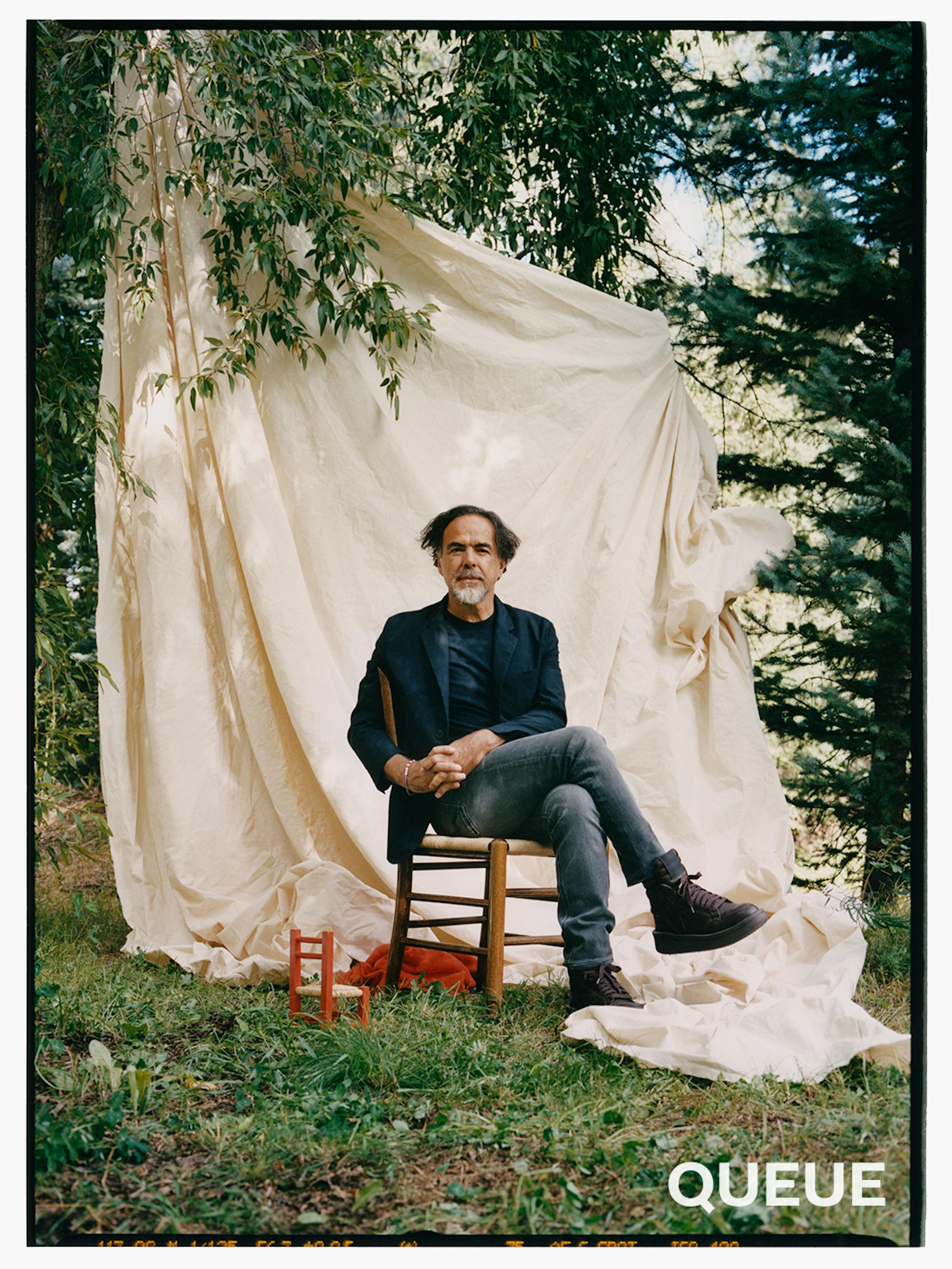 Alejandro González Iñárritu sits in a small chair against a white sheet.