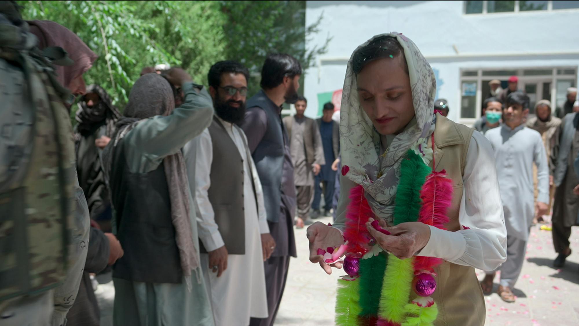 Zarifa Ghafari holds some neon feathers surrounded by a bunch of people.