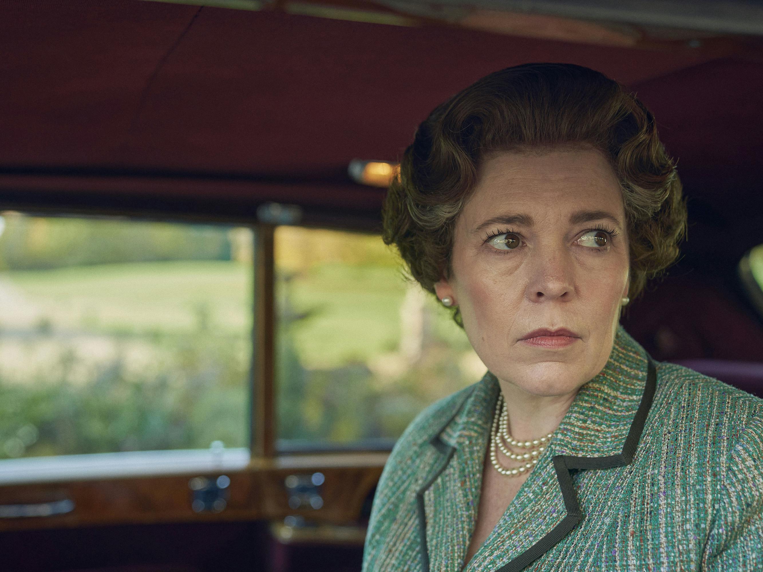 Queen Elizabeth (Olivia Colman) wears a green suit and peeks out from the car window