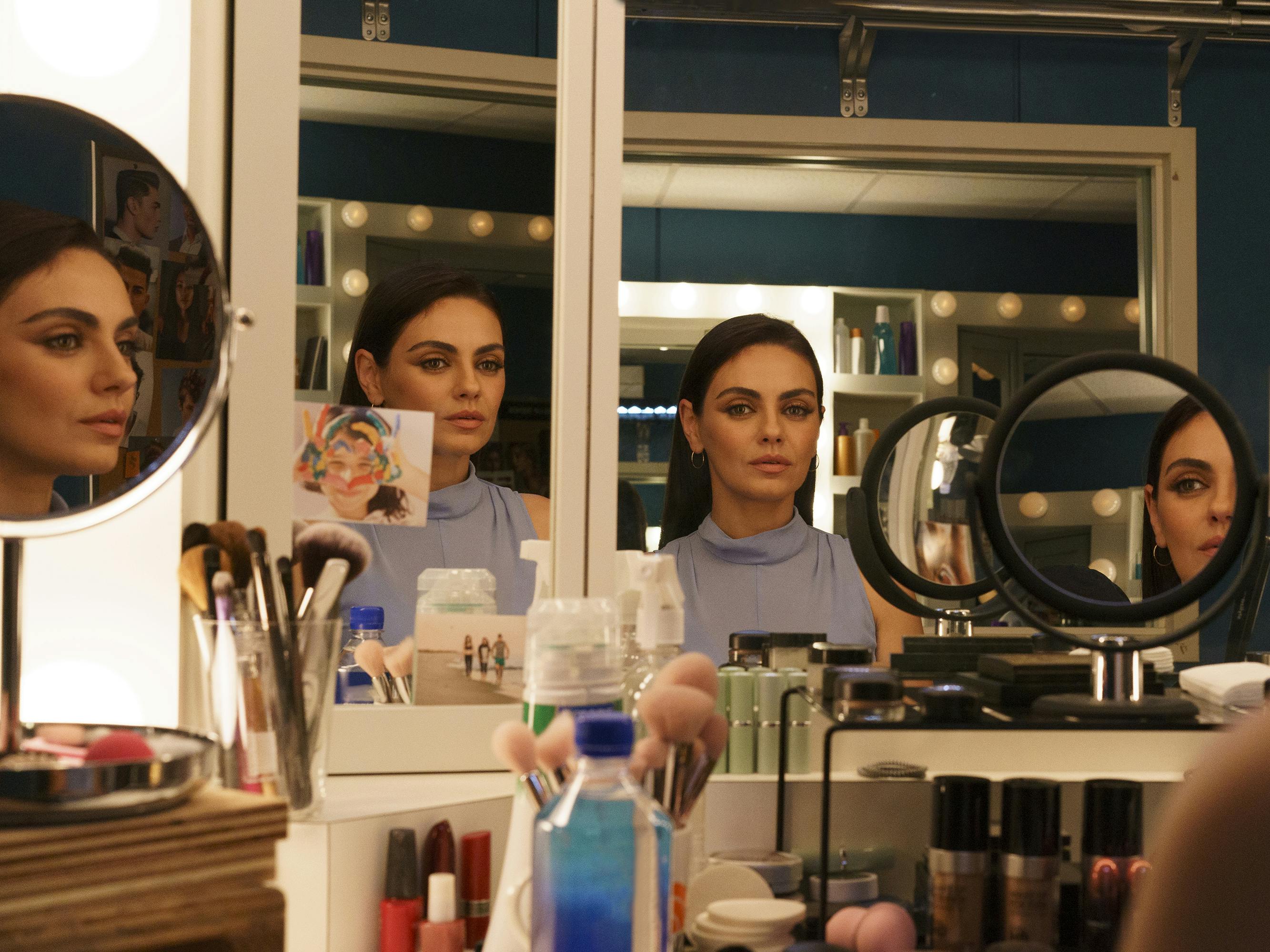Mila Kunis wears a blue top and looks at many reflections of herself in many different mirrors at a makeup vanity. This meta-cinematic image ran as a digital cover for Queue.  