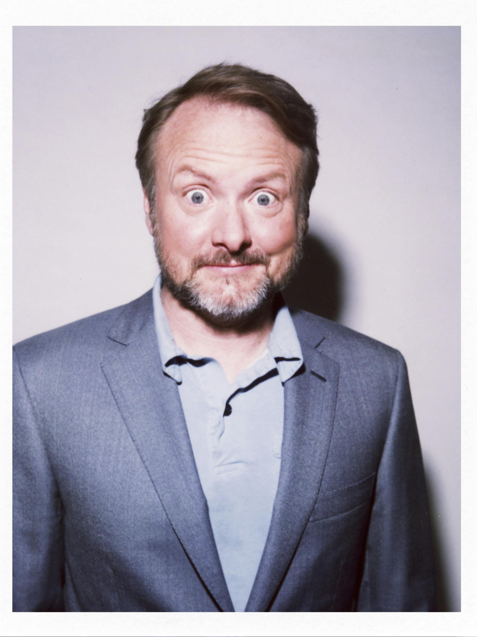 Rian Johnson wears a grey shirt and dark grey blazer and looks shocked on this digital cover.