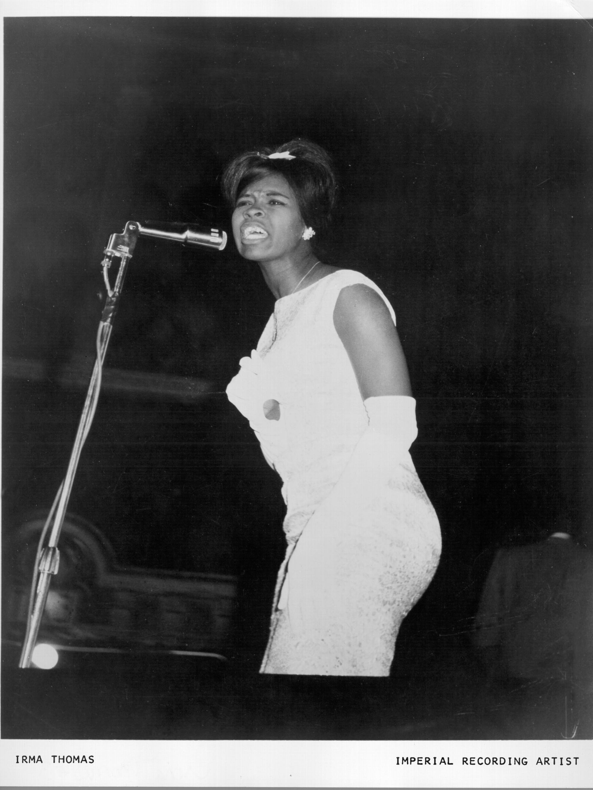Irma Thomas wears a fabulous white dress and gloves and sings into a mic.