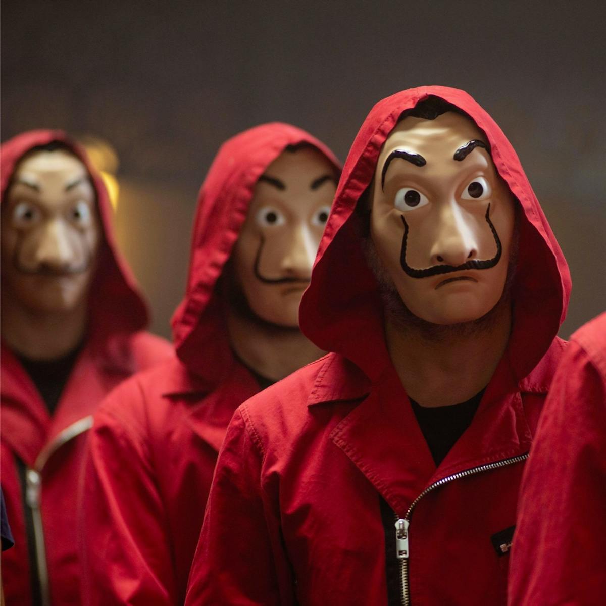 People in red jackets wearing masks walk in a line. They have dark eyebrows and mustaches, and alarmed expressions.