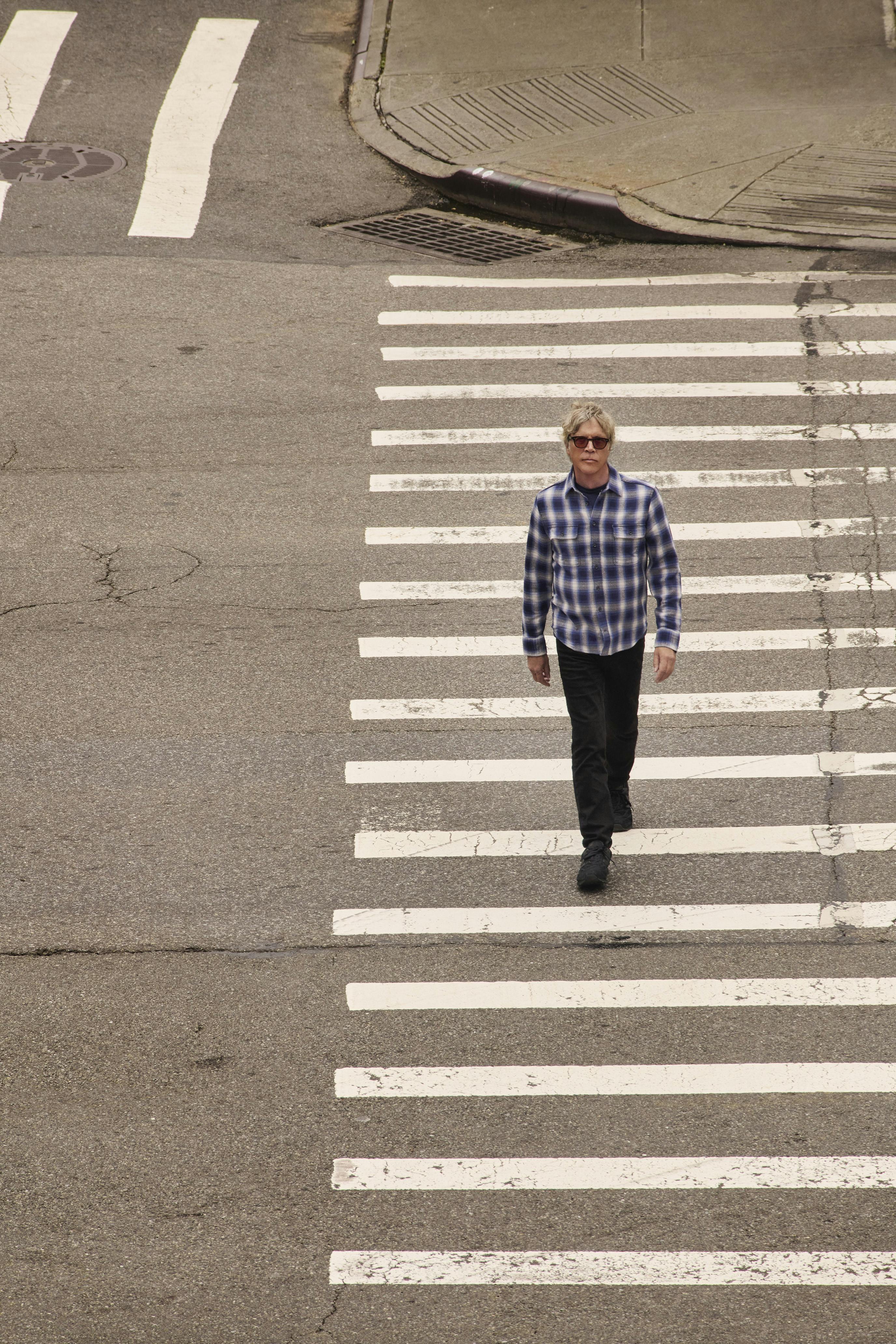 Todd Haynes walks on a sidewalk in a flannel shirt and black pants. 