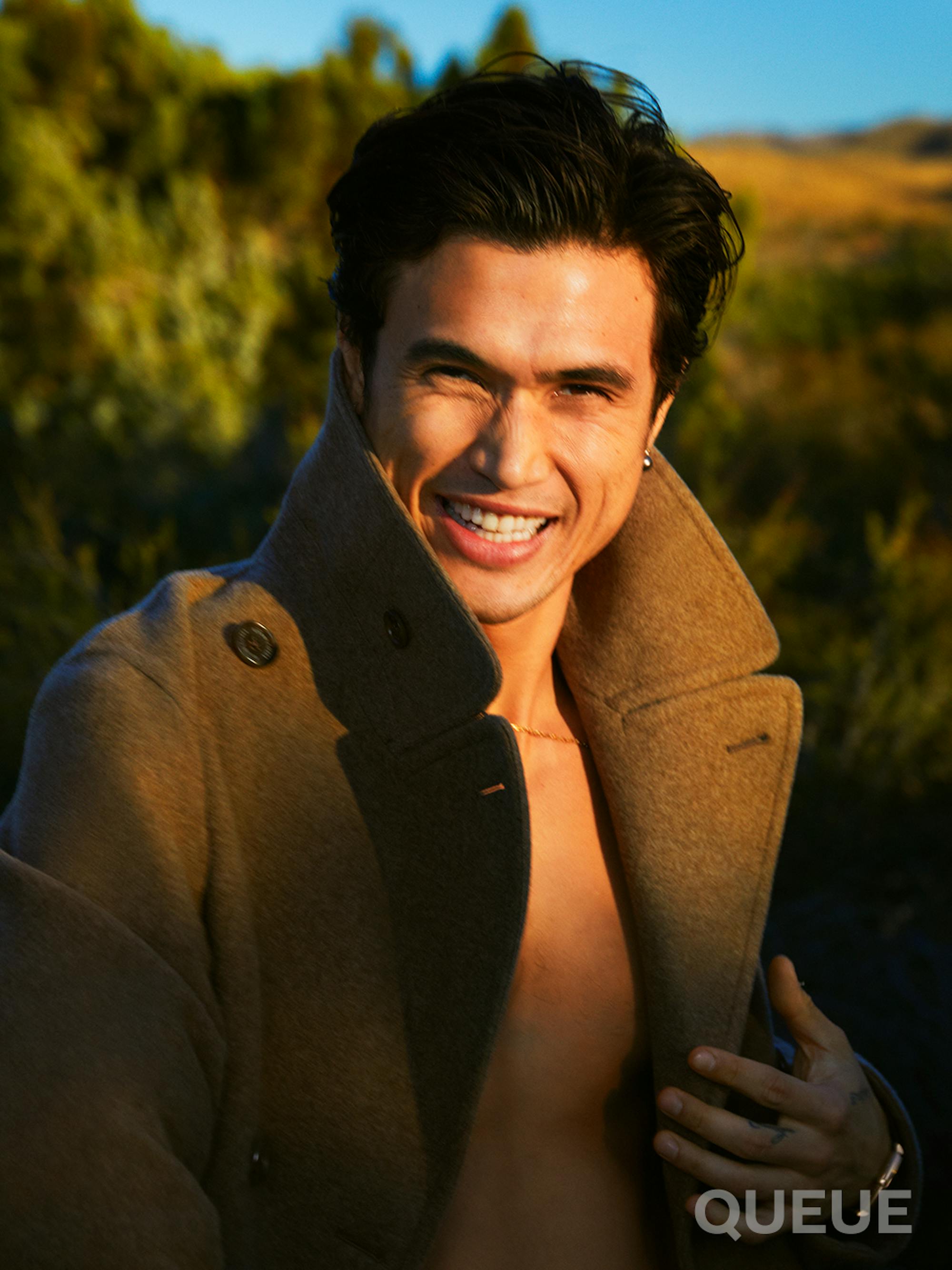 Charles Melton lets loose with a smile and his jacket collar popped.