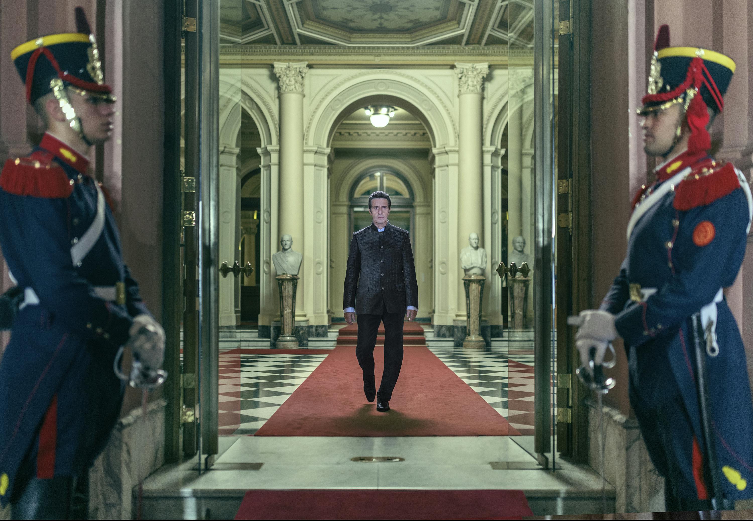 Emilio (Diego Peretti) walks down a red carpet through an open door, at which two guards stand in full uniform.