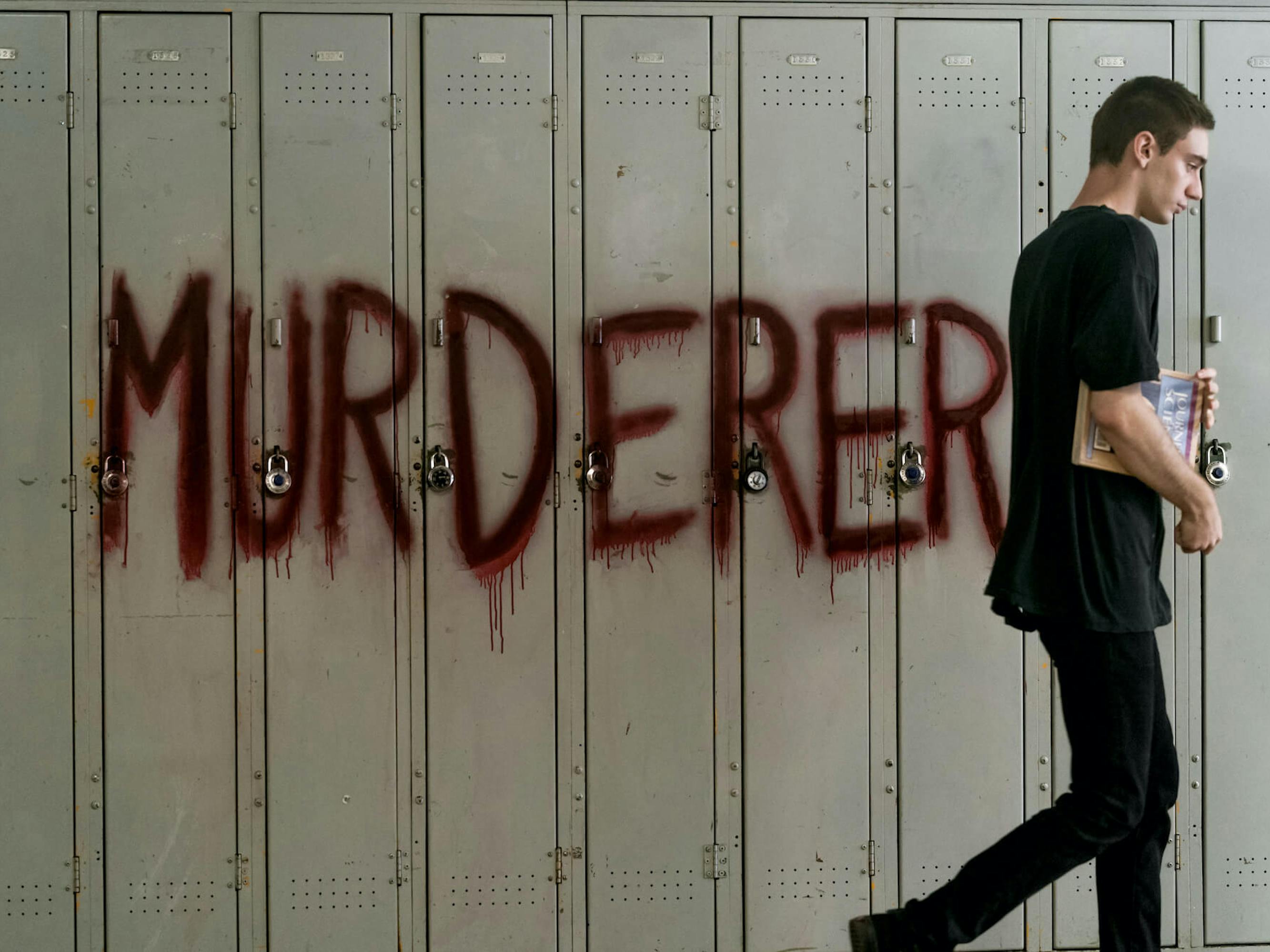 Ollie Larsson (Théodore Pellerin) wears all black and walks past lockers spray painted ‘Murderer’ in red.