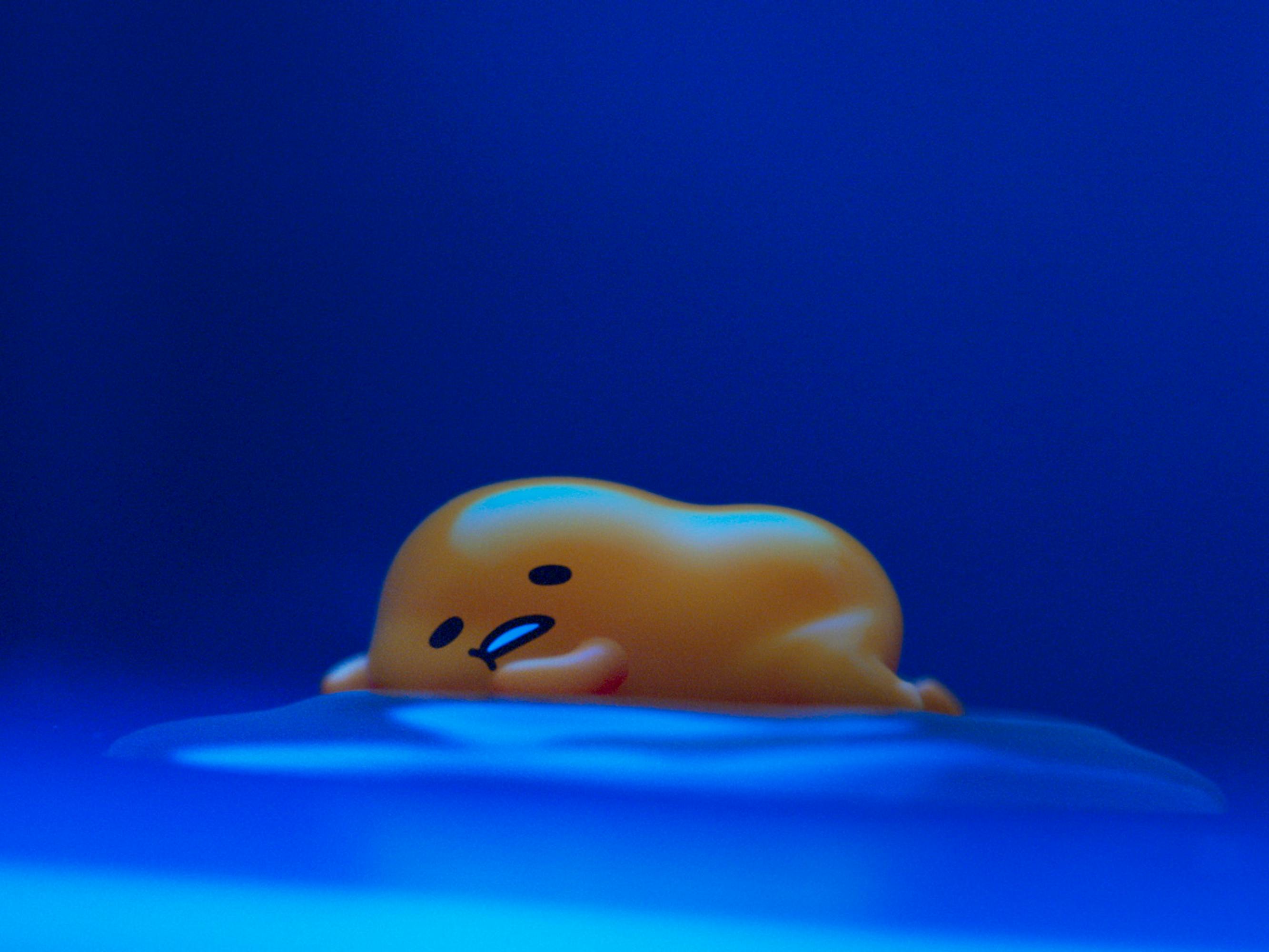 Gudetama rests on an egg white against a blue background.