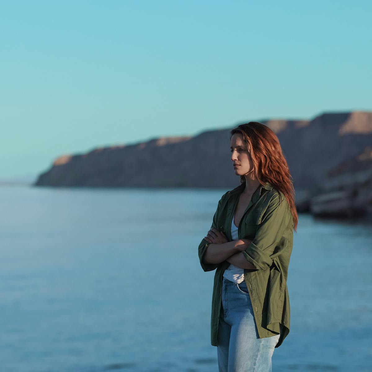Sarah (Dianna Agron) wears a green jacket and stands by a beautiful blue ocean.