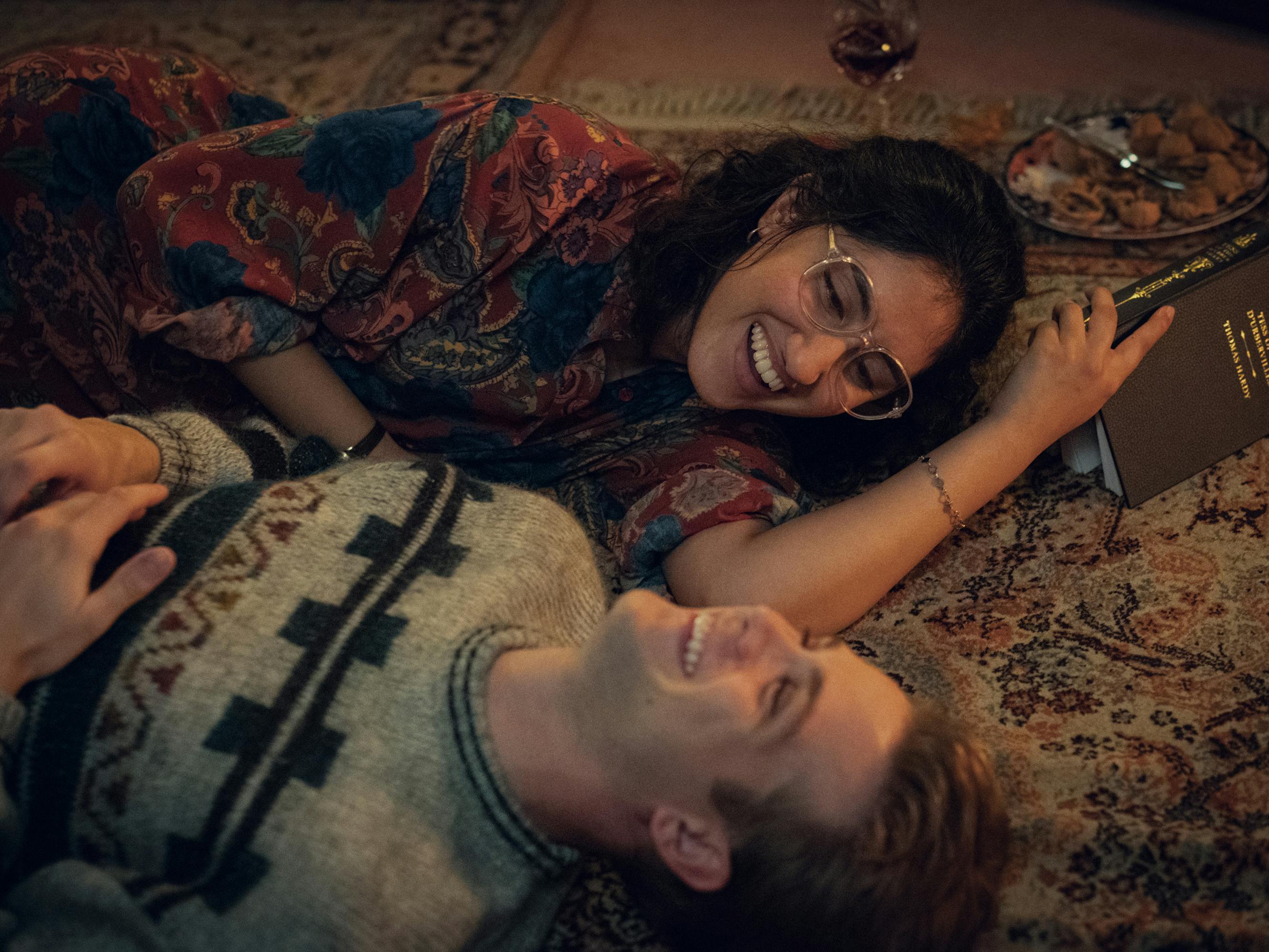 Dexter Mayhew (Leo Woodall) and Emma Morley (Ambika Mod) lie on a patterned rug laughing.