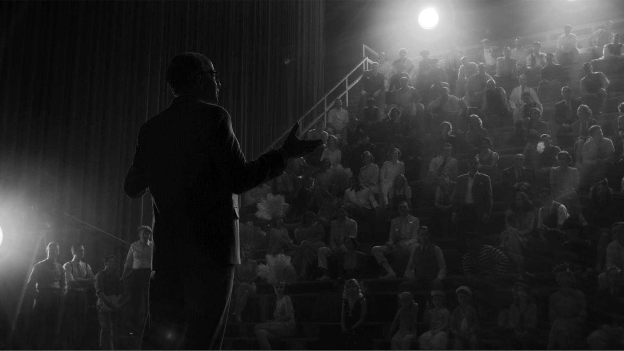 In a shot from the film, we see how the scene above translates to a black-and-white experience. The spotlights around the theater are like small suns.