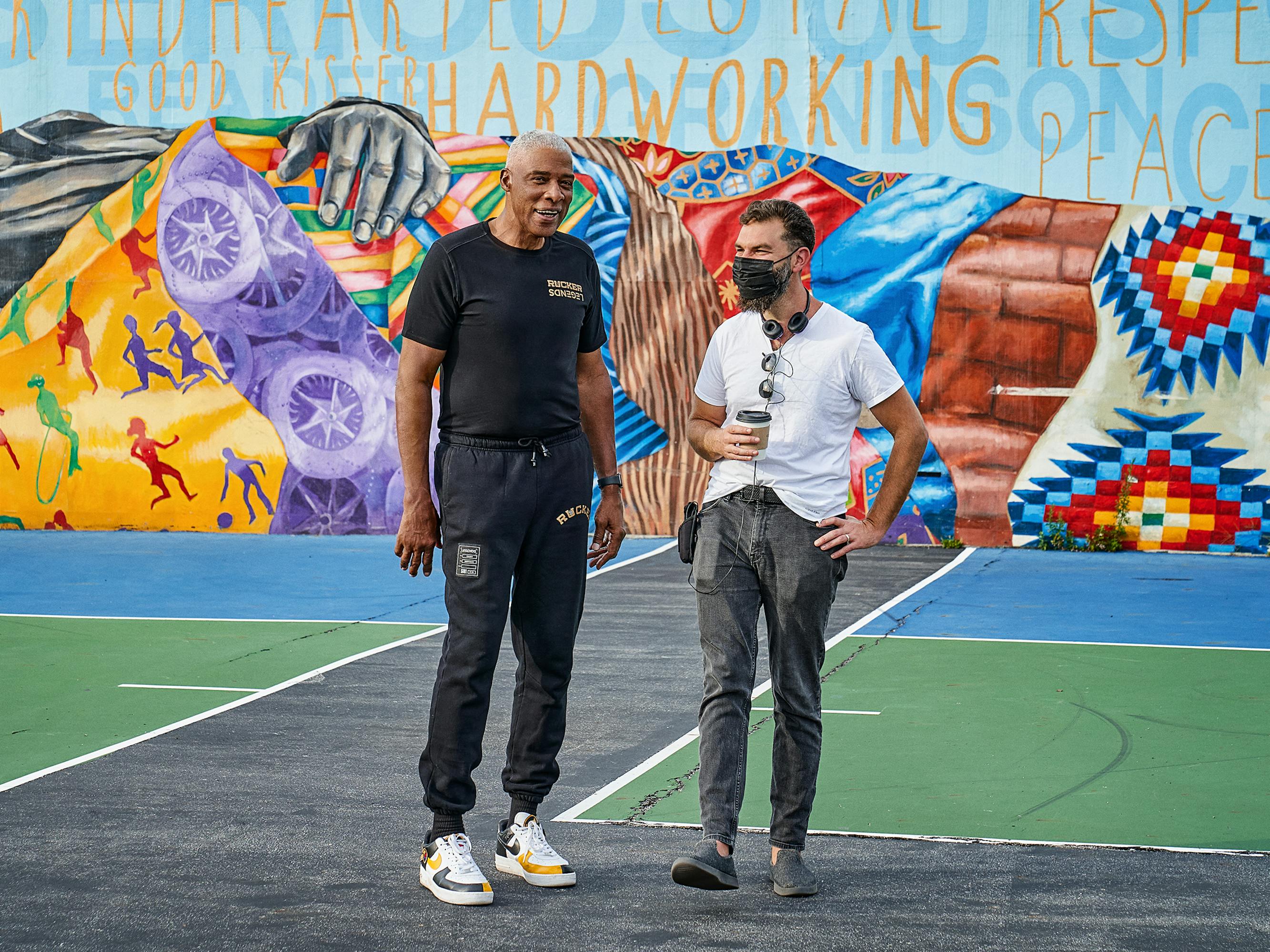 Dr. J and Jeremiah Zagar stand on a court decorated by a colorful mural.