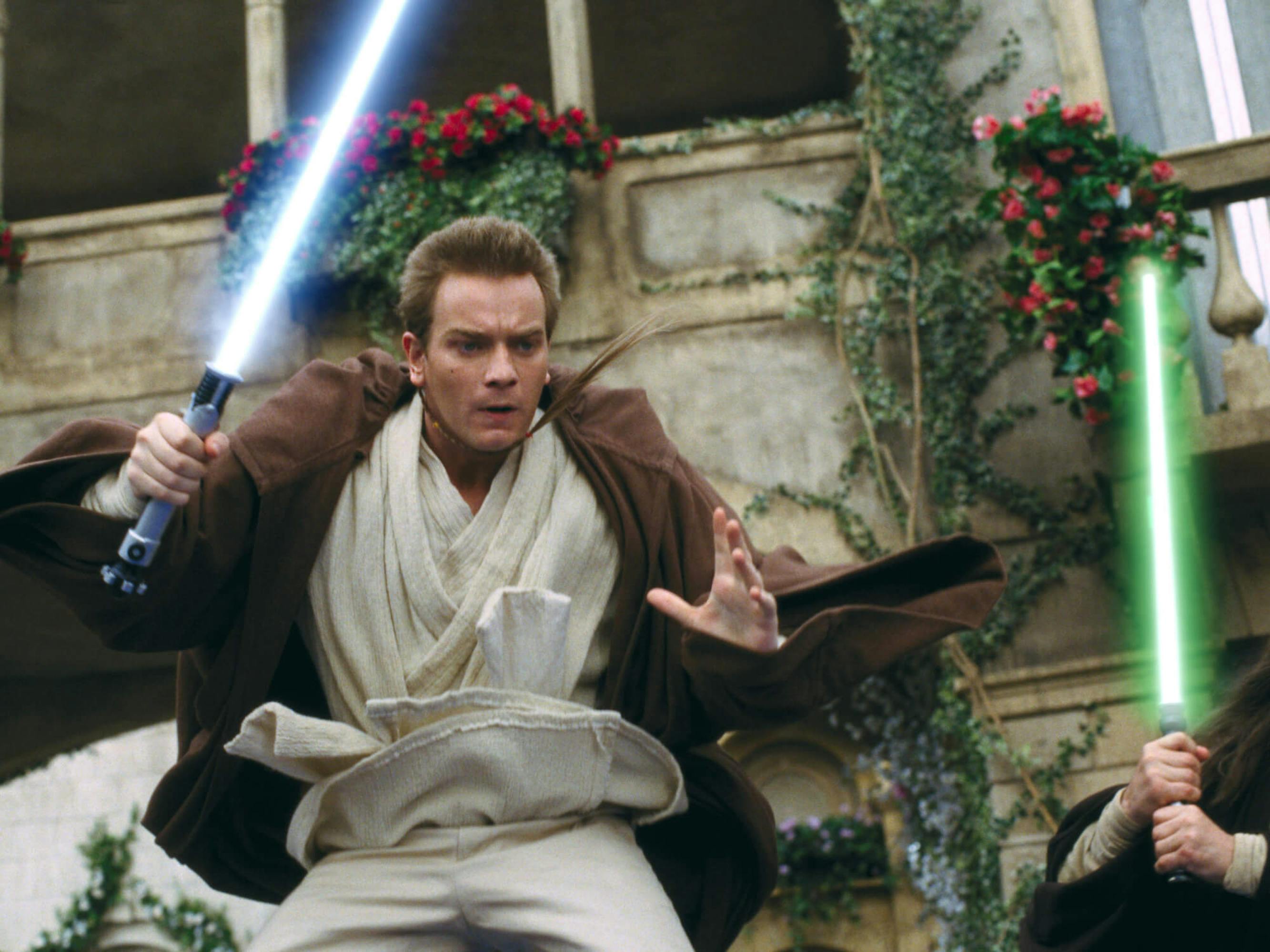 Obi-Wan Kenobi (Ewan McGregor) in Star Wars: Episode I - The Phantom Menace wears light colored robes as he jumps into action holding his lightsaber.