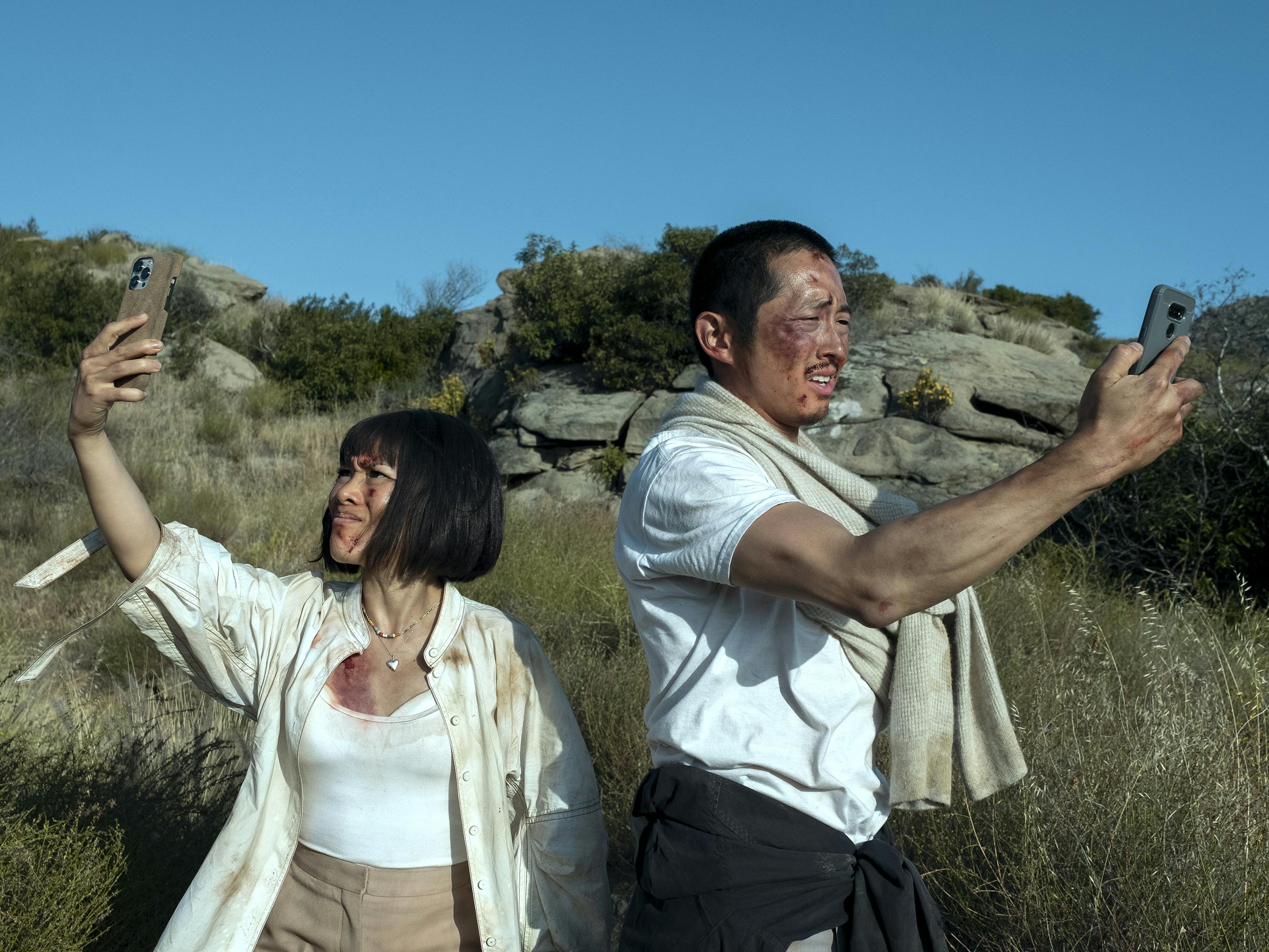 Amy Lau (Ali Wong) and Danny Cho (Steven Yeun) look disheveled and dirty in the middle of the desert, holding their phones up to a very blue sky.  
